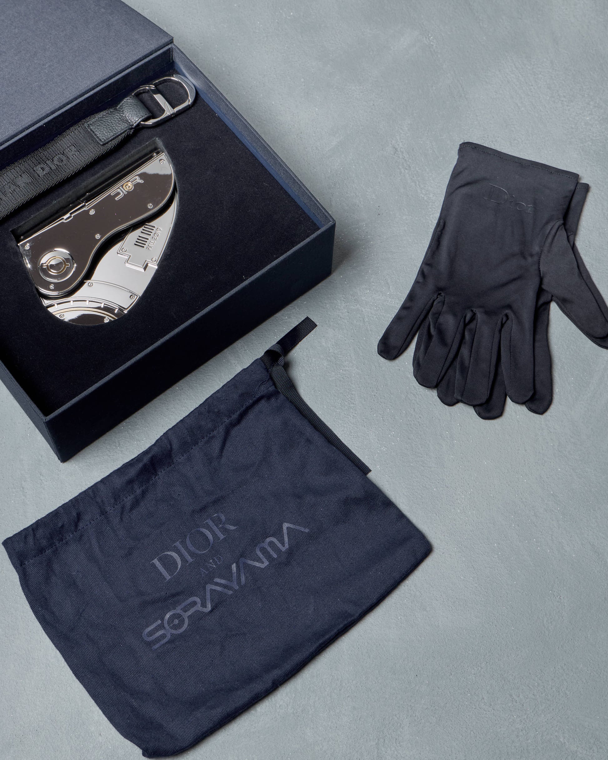 Silver Dior mini saddle bag, gloves, and branded cloth on a gray surface