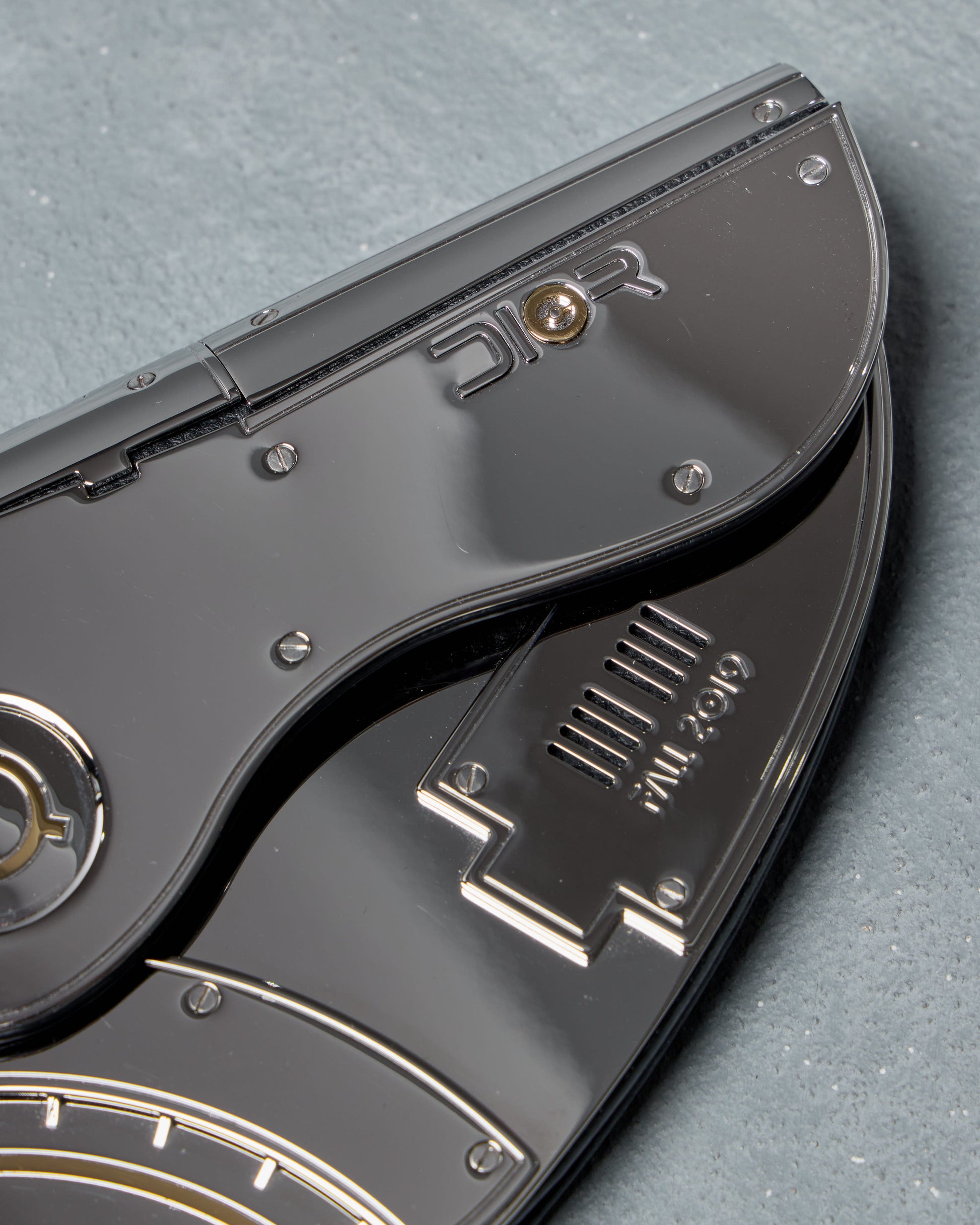 Close-up of a silver Dior mini clutch bag 'DIOR' branding on a gray background