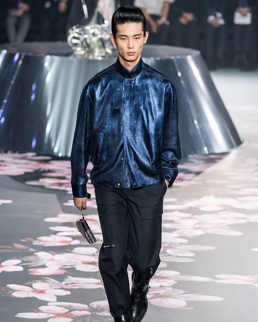 Man walking on a Dior runway wearing a blue jacket and black pants.