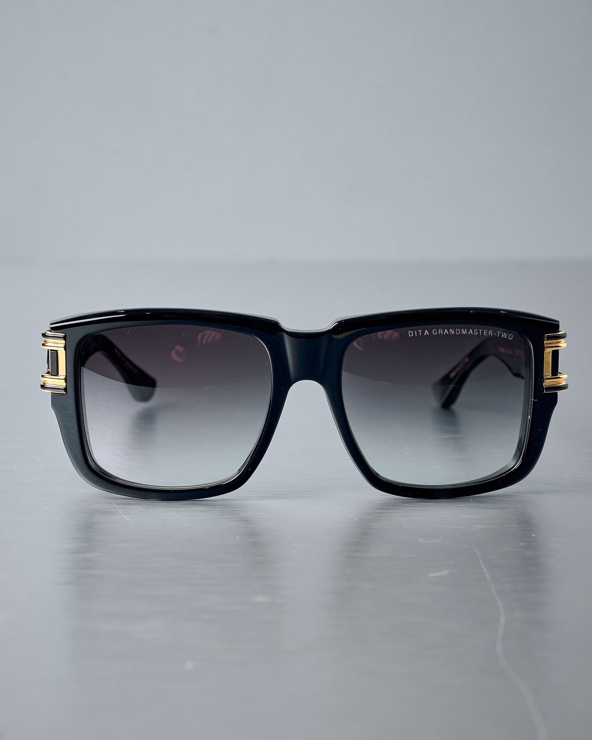 Black Dita sunglasses with gold accents on a grey background