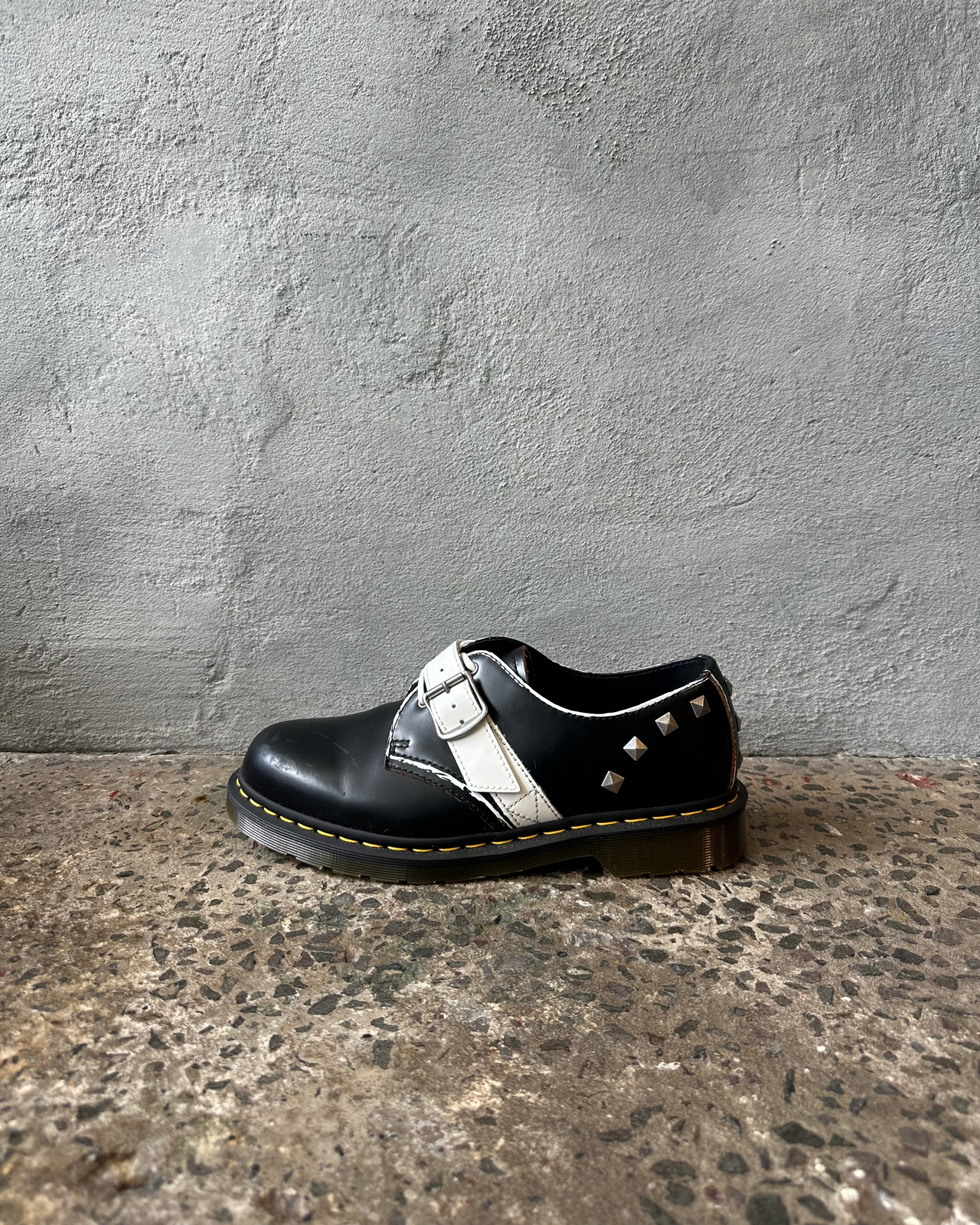 Black leather doc martens shoe with white laces on a textured surface and gray wall background