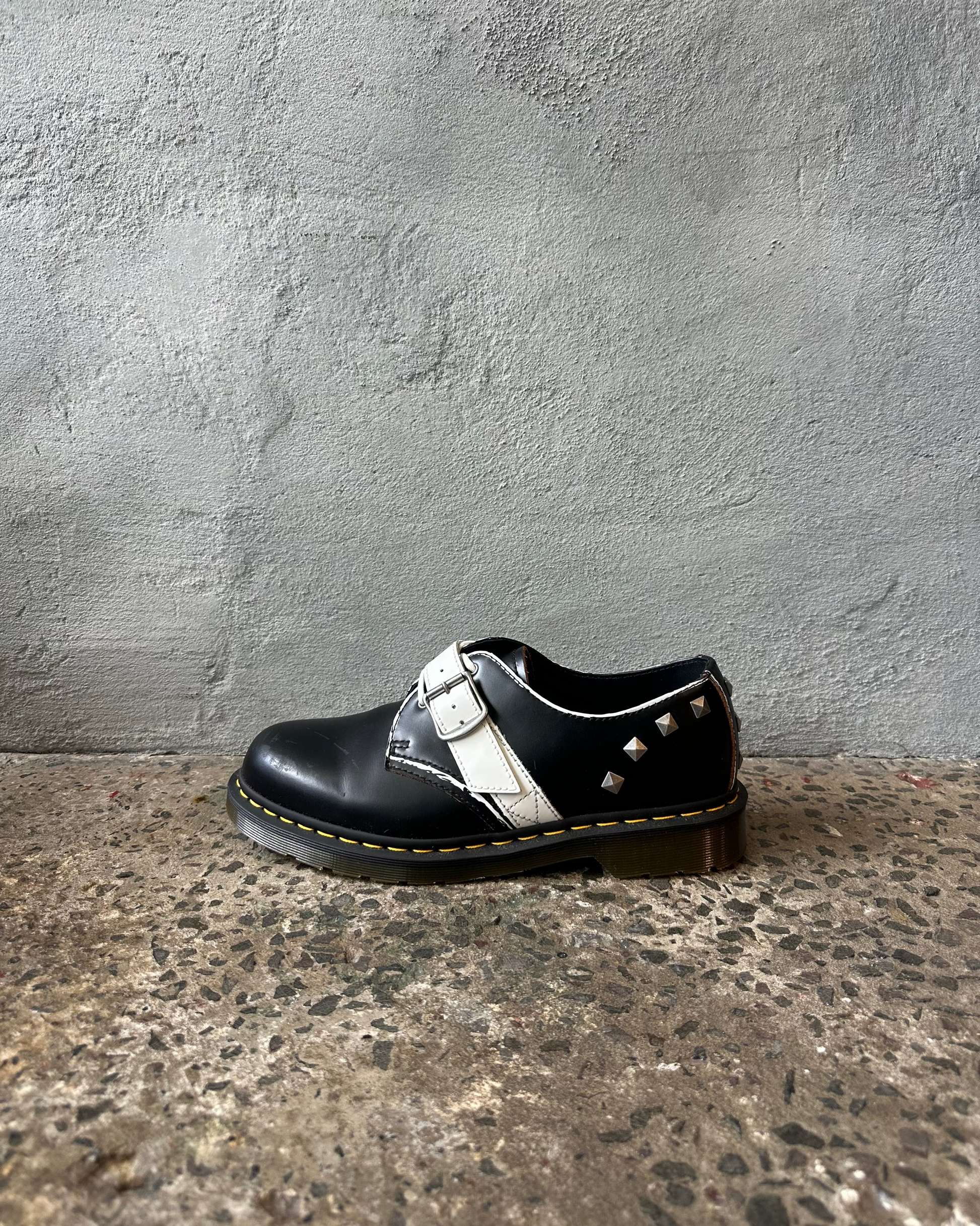 Black leather doc martens shoe with white laces on a textured surface and gray wall background