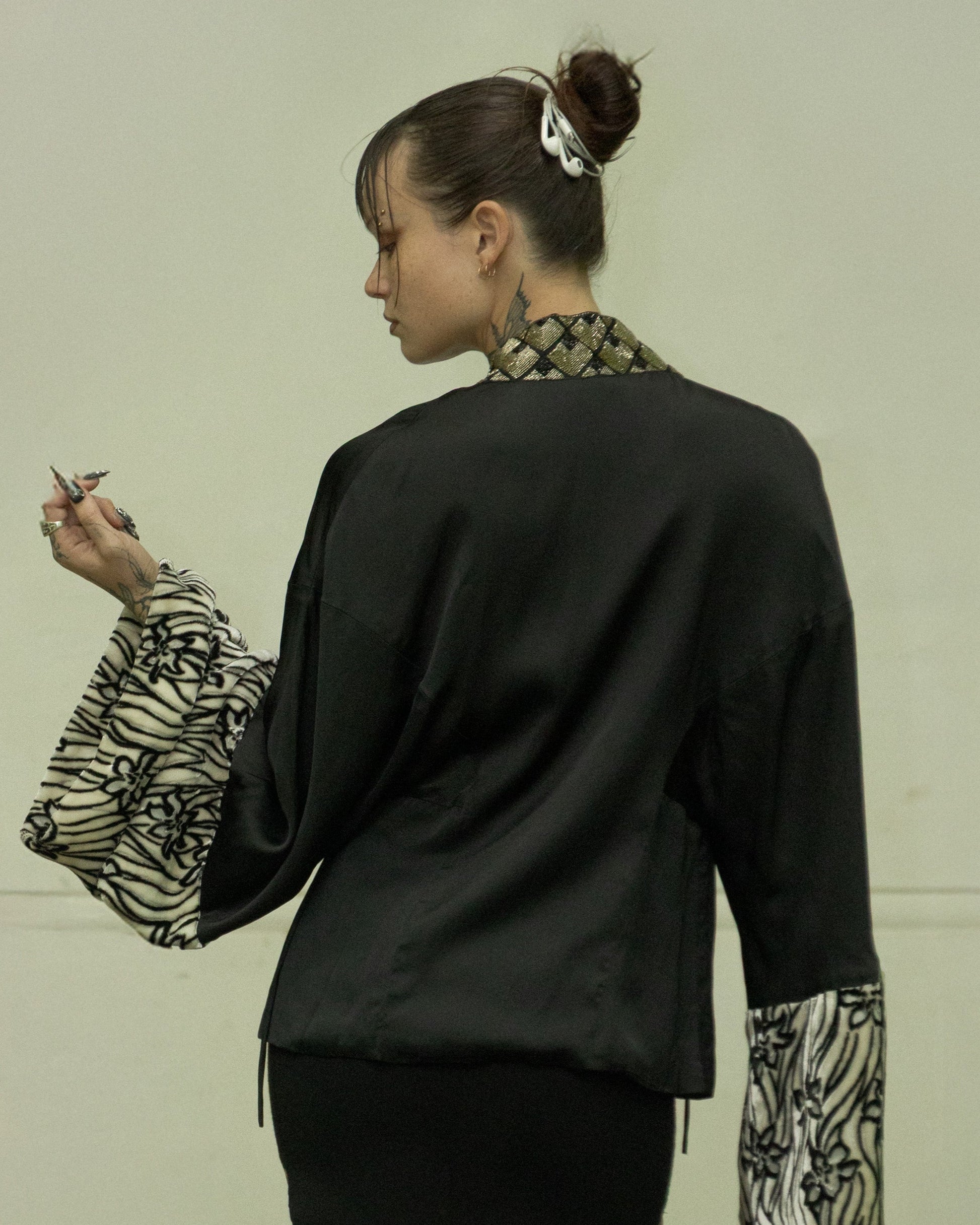 Person standing in a garage with a vintage car and colourful wall in the background wearing a beaded Dries Van Noten beaded kimono top. 