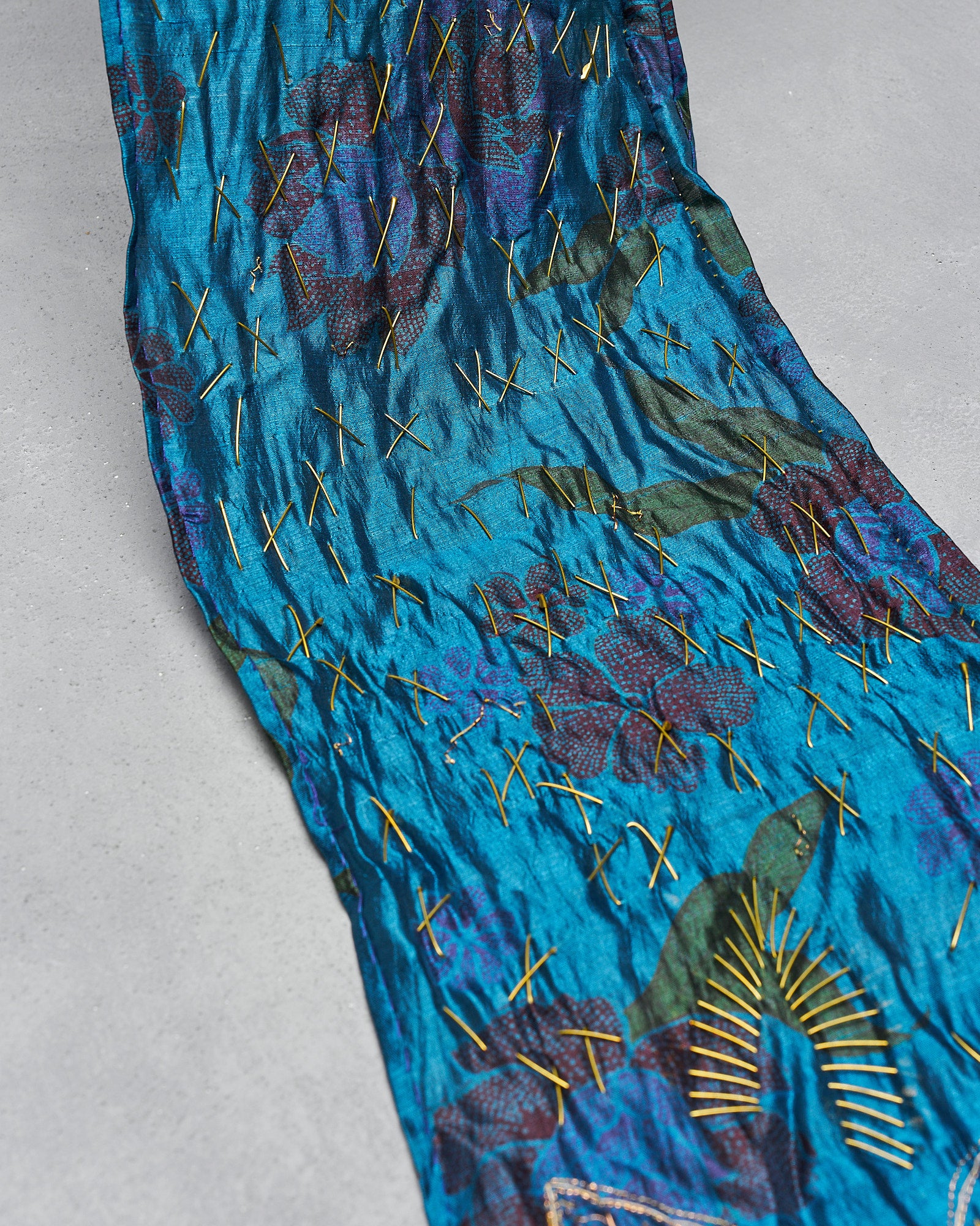 A vibrant blue Dries Van Noten textile with abstract floral patterns features gold cross-stitch details. 