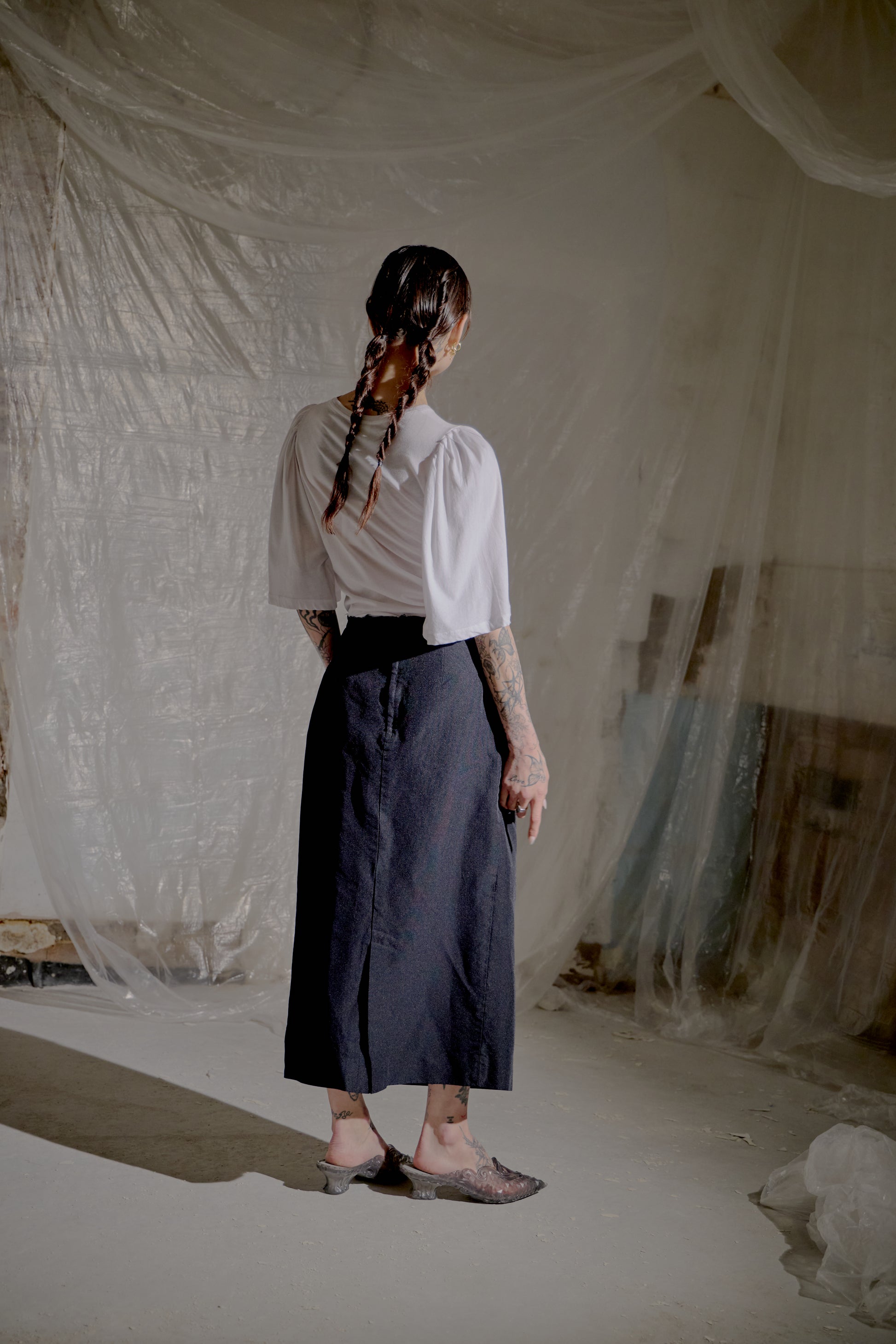 Person wearing a white Dries Van Noten blouse and dark skirt standing in a room with draped fabric.