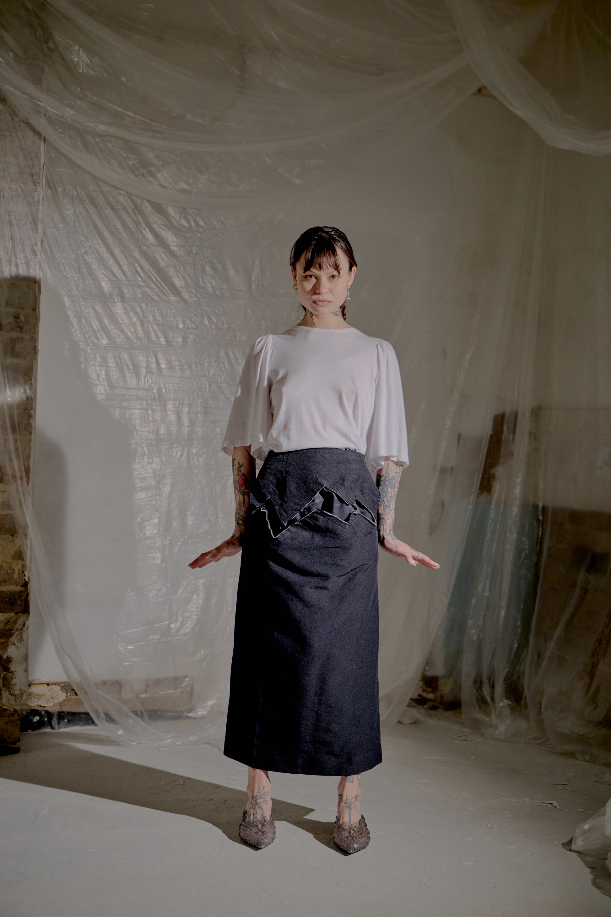 Person wearing a white Dries Van Noten top and black skirt in a room with draped fabric.