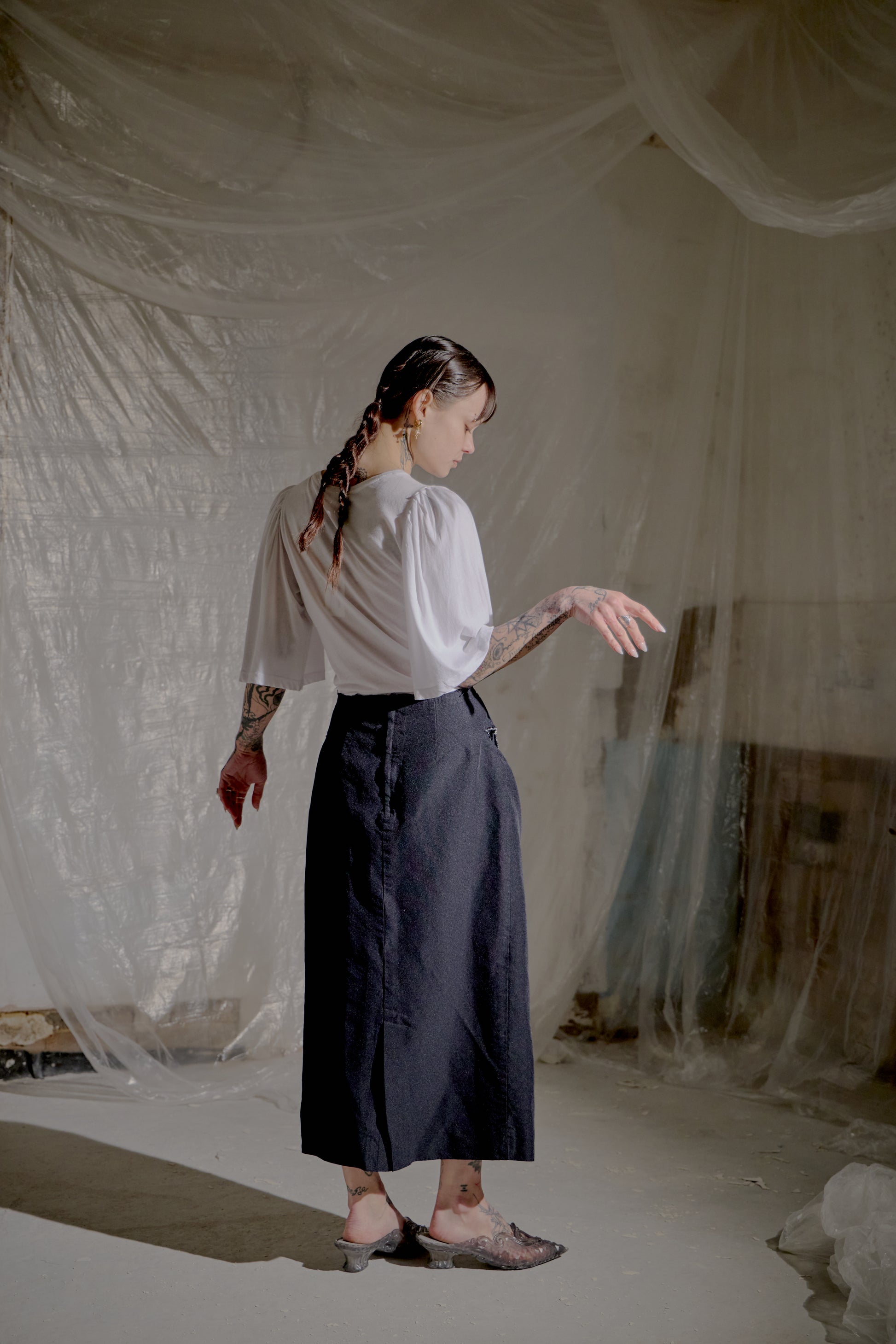 Person wearing a white Dries Van Noten blouse and dark skirt in a softly lit room with draped fabric.