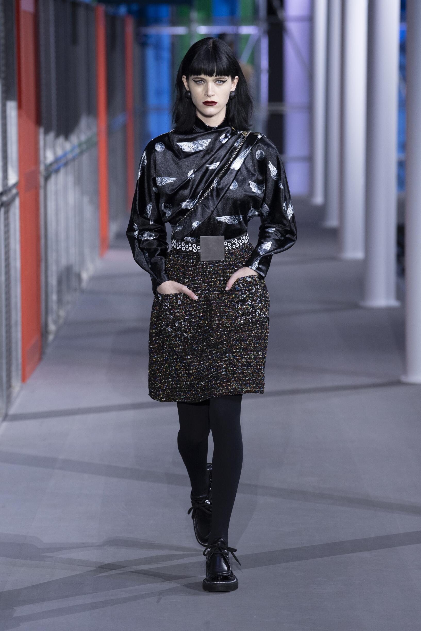 Model wearing a black and white outfit with a sequin skirt in a Louis Vuitton fashion show setting.