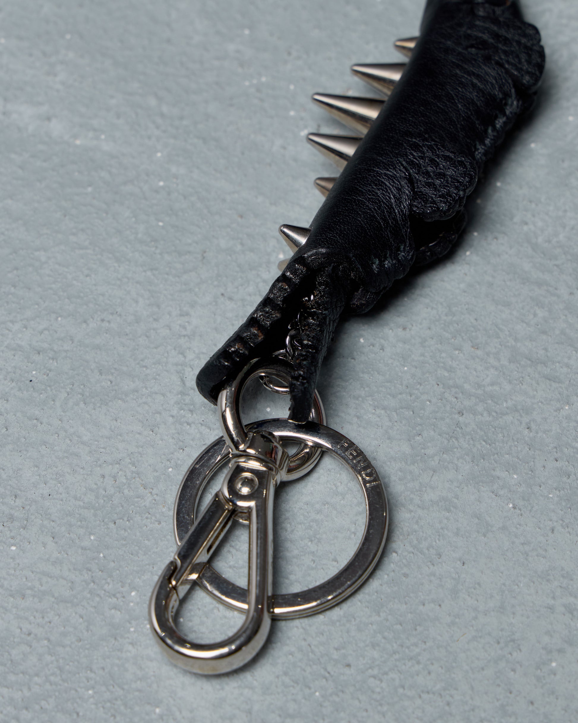 Black leather Fendi keychain with metal spikes and keyring on a gray background