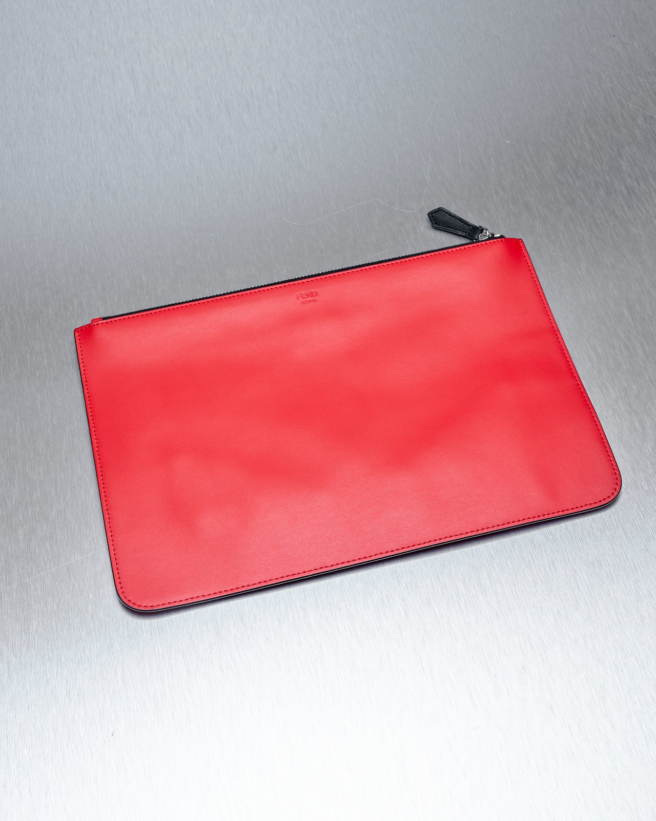 A flat leather Fendi clutch with a silver top-zip and bold black eyes with silver-studded pupils on a reflective surface.