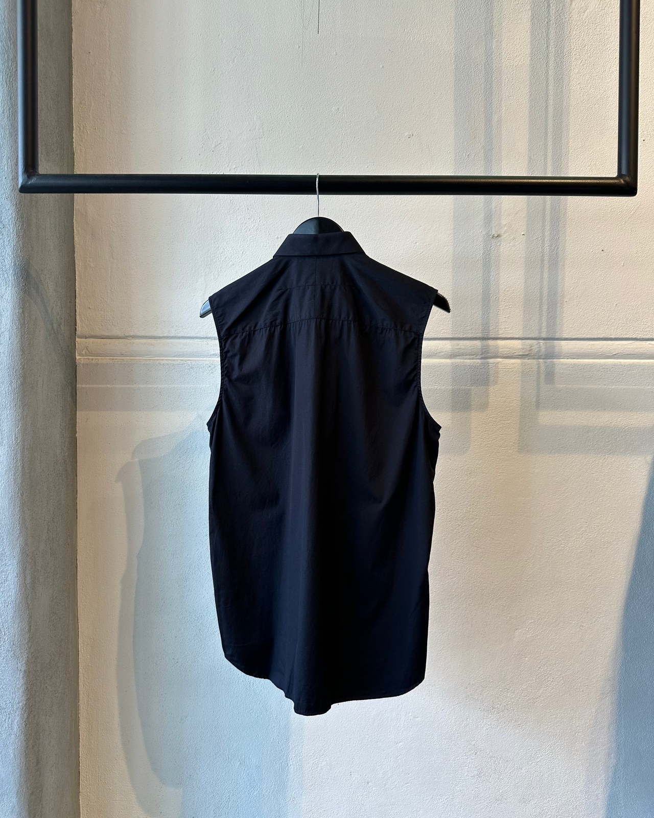 Black sleeveless Givenchy shirt hanging on a rack against a neutral wall.