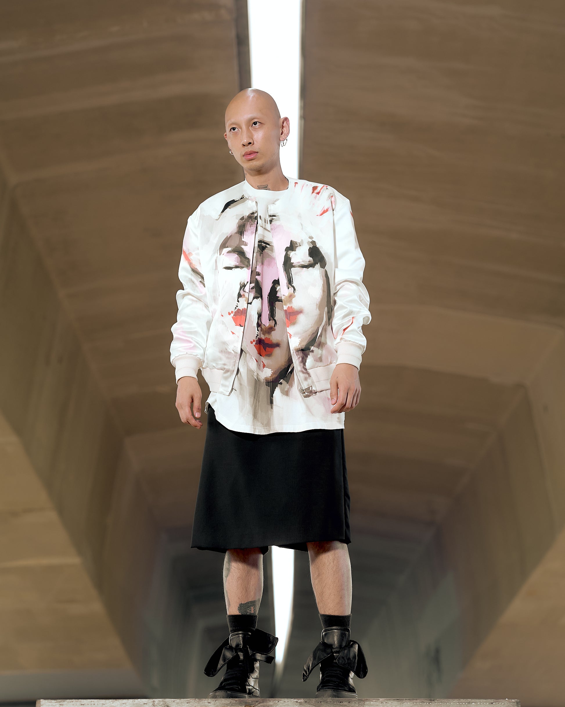 A model wearing a white satin Givenchy bomber jacket with a sublimation print of the Virgin Mary, paired with a black skirt and black shoes.