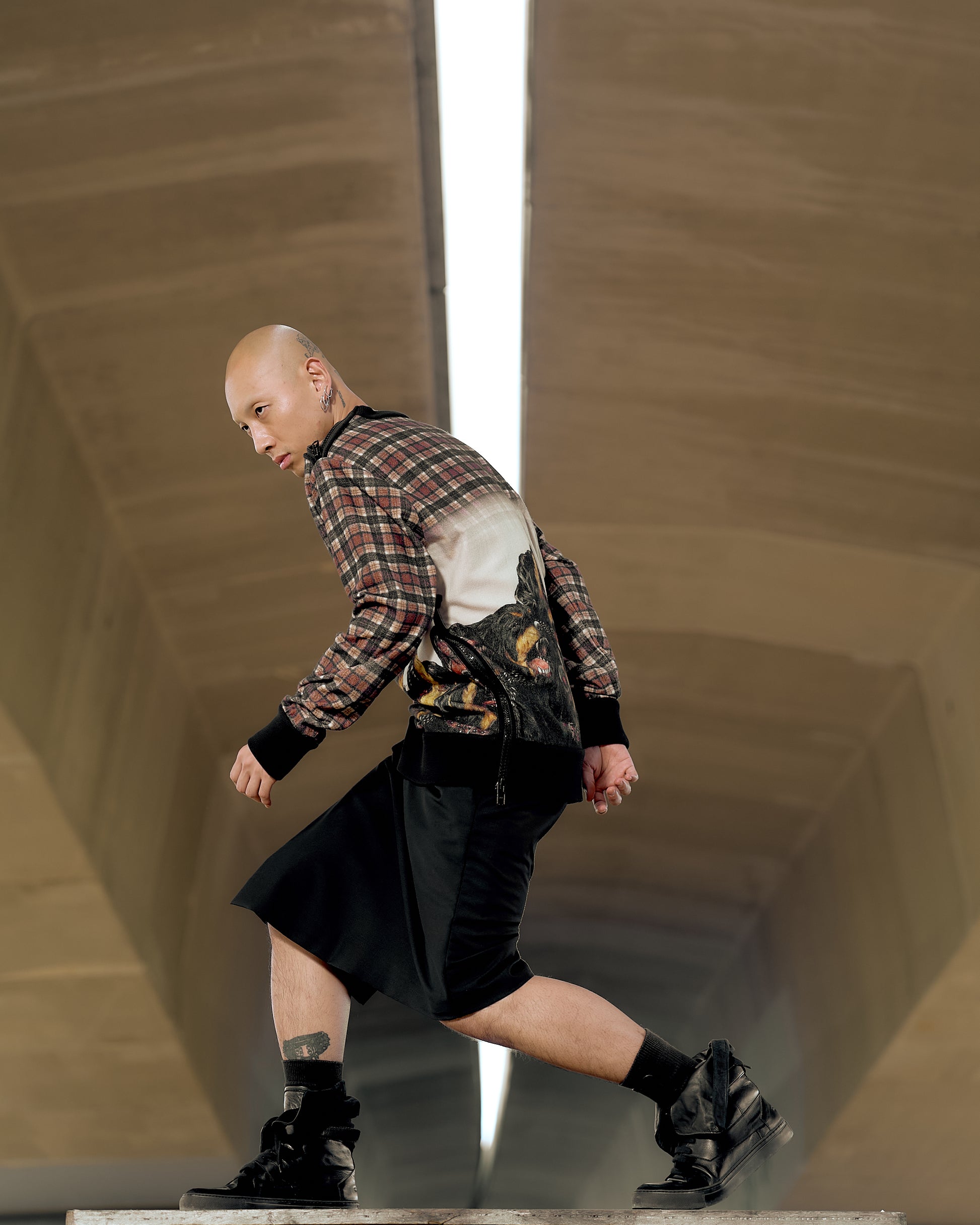 A person confidently walks in a modern space, wearing a patterned Givenchy shirt, black skirt, and boots. The setting feels futuristic with a bright, central light.