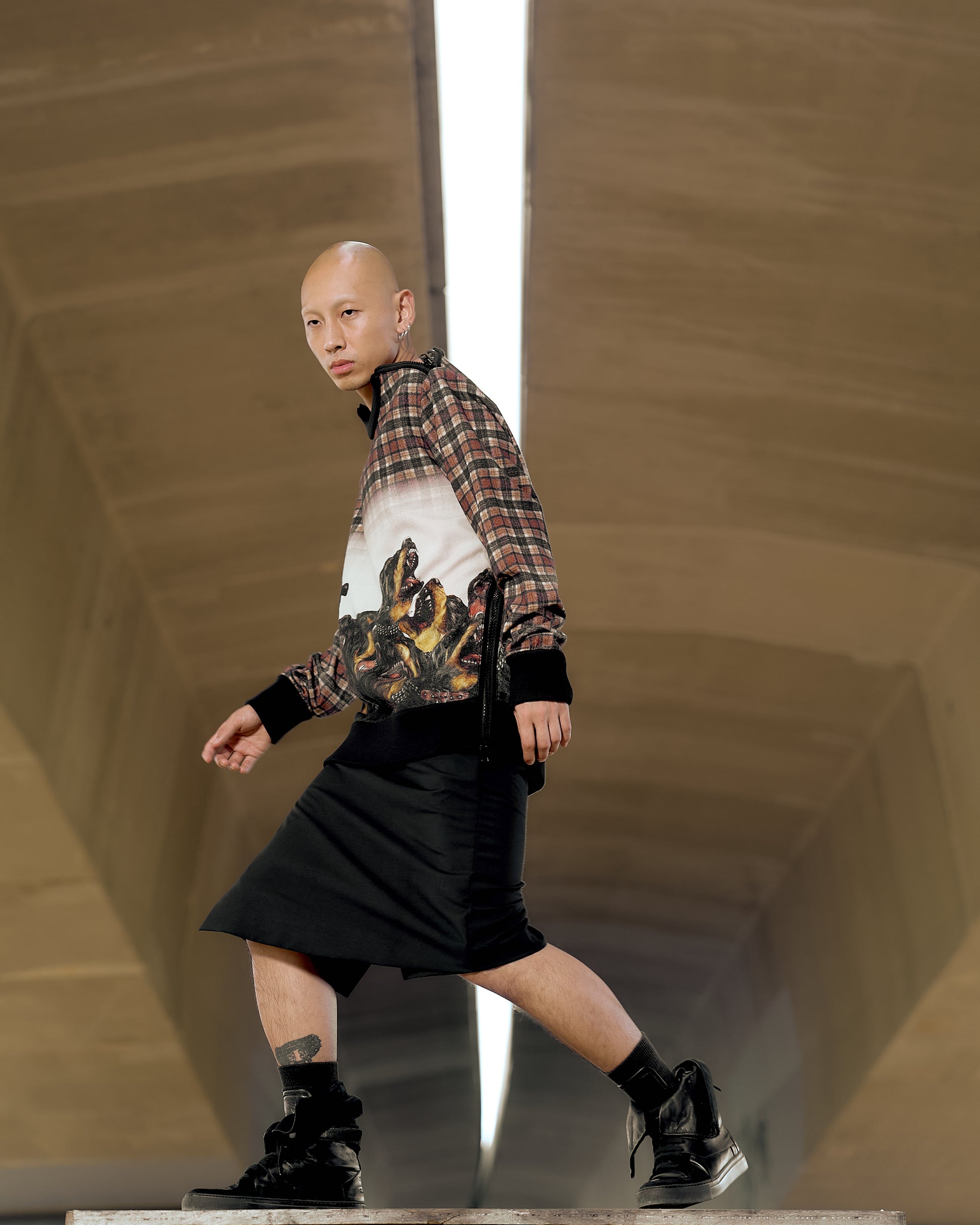 A person confidently walks in a modern space, wearing a patterned Givenchy shirt, black skirt, and boots. 