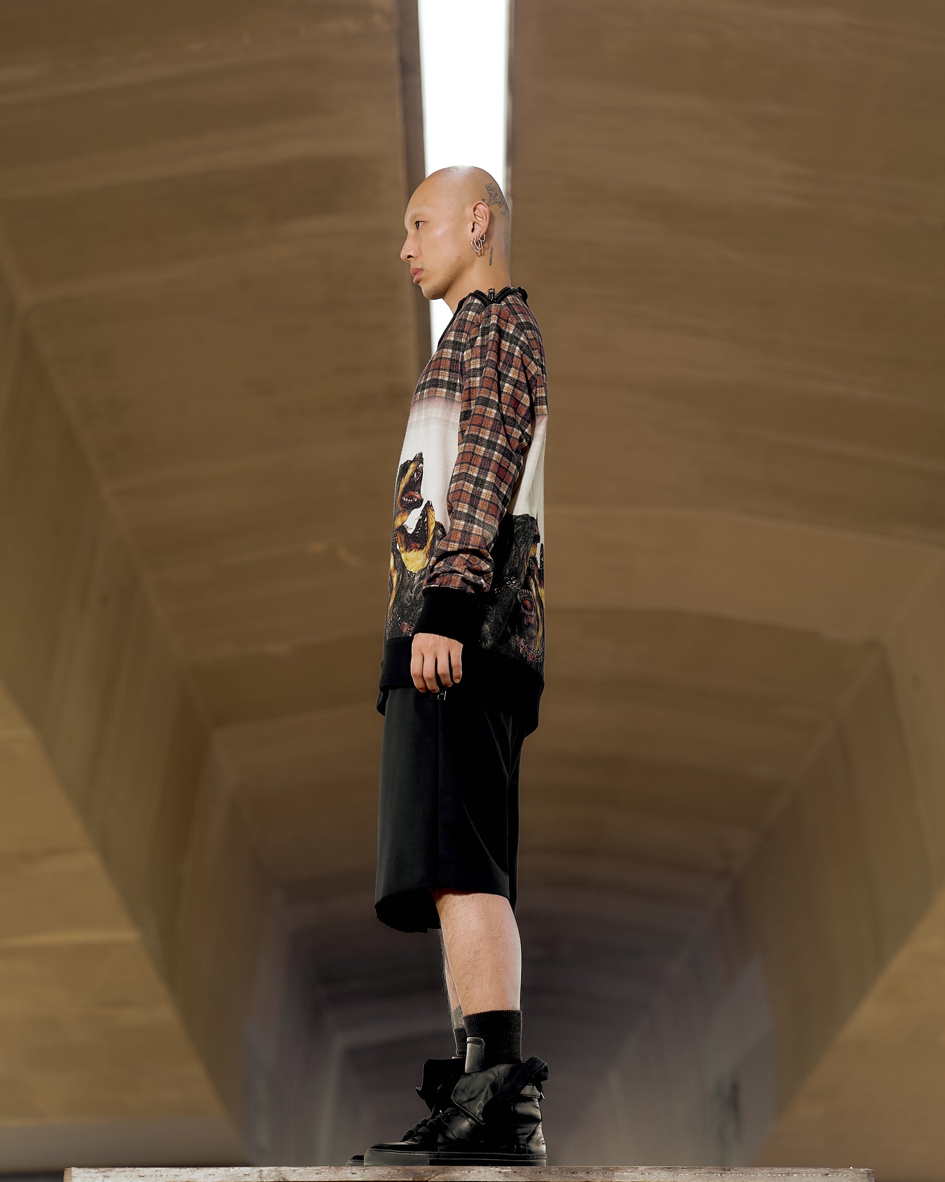A model stands on a runway, wearing a plaid Givenchy sweatshirt with artistic patterns and black shorts. 