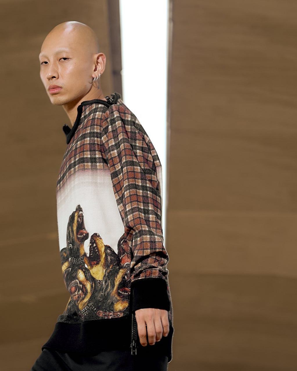 Bald model in a plaid Givenchy shirt with an abstract animal print walks on a runway. 