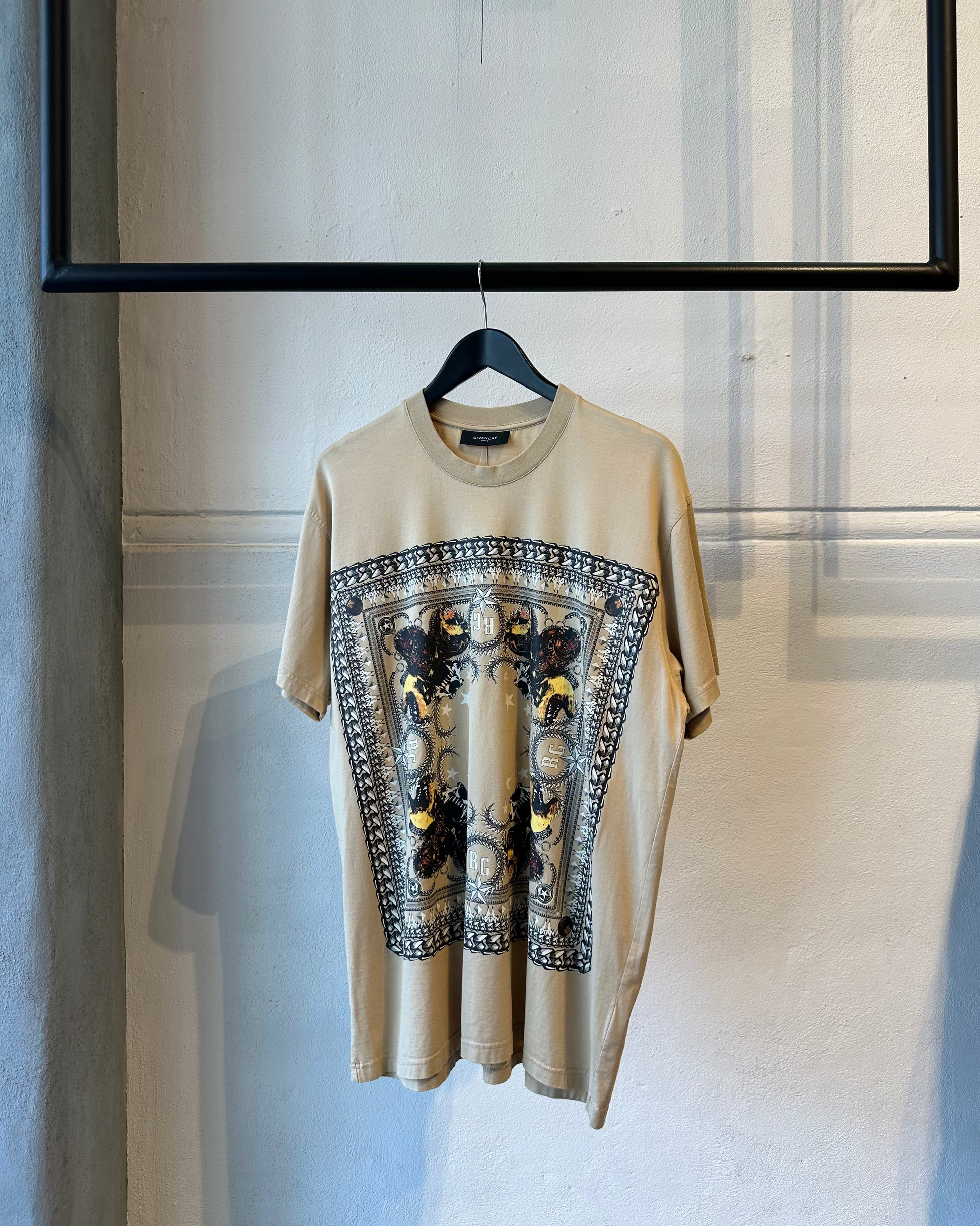 Beige Givenchy t-shirt with a graphic design on a hanger against a neutral wall.