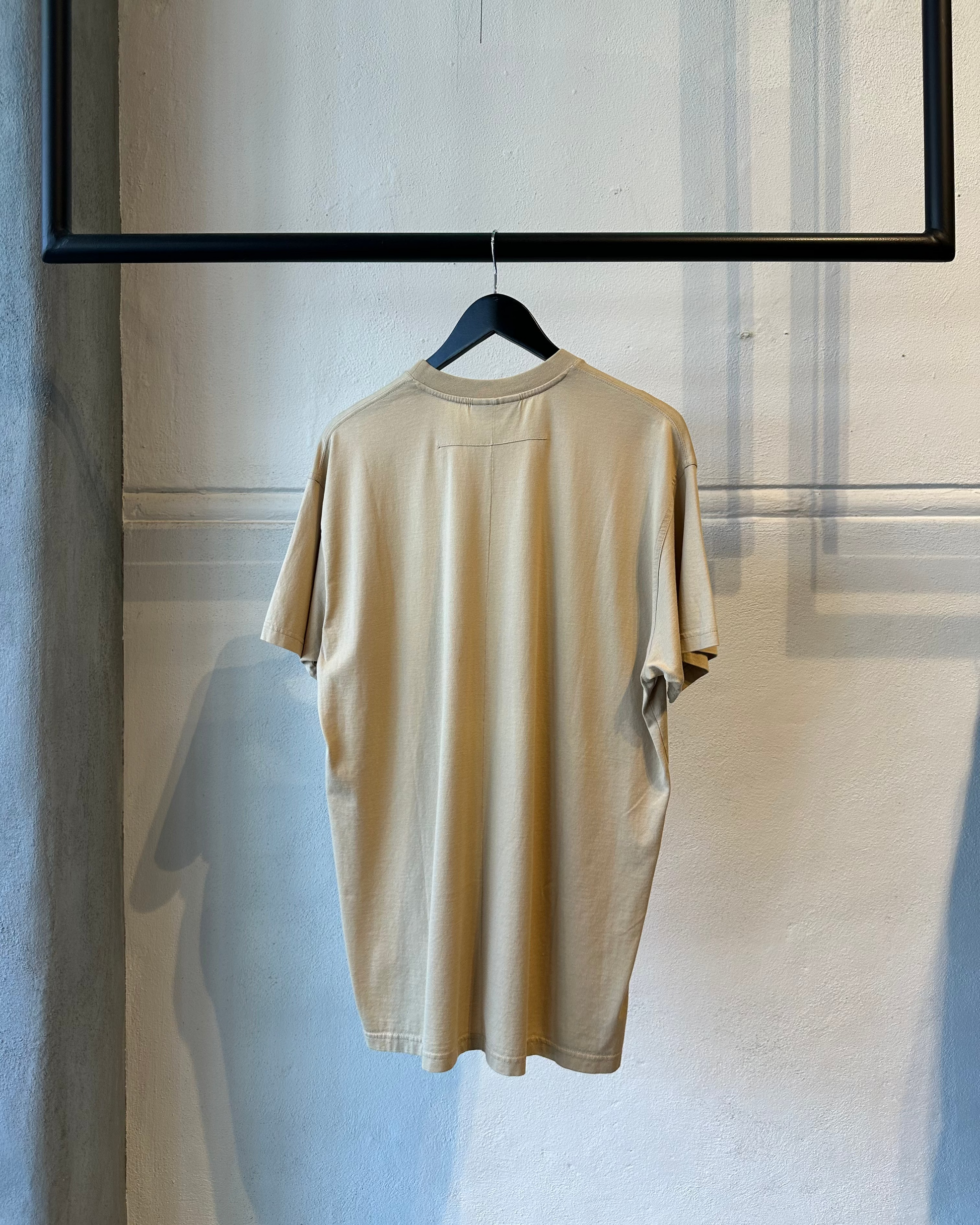 Reverse of a beige Givenchy t-shirt hanging on a hanger against a neutral wall.
