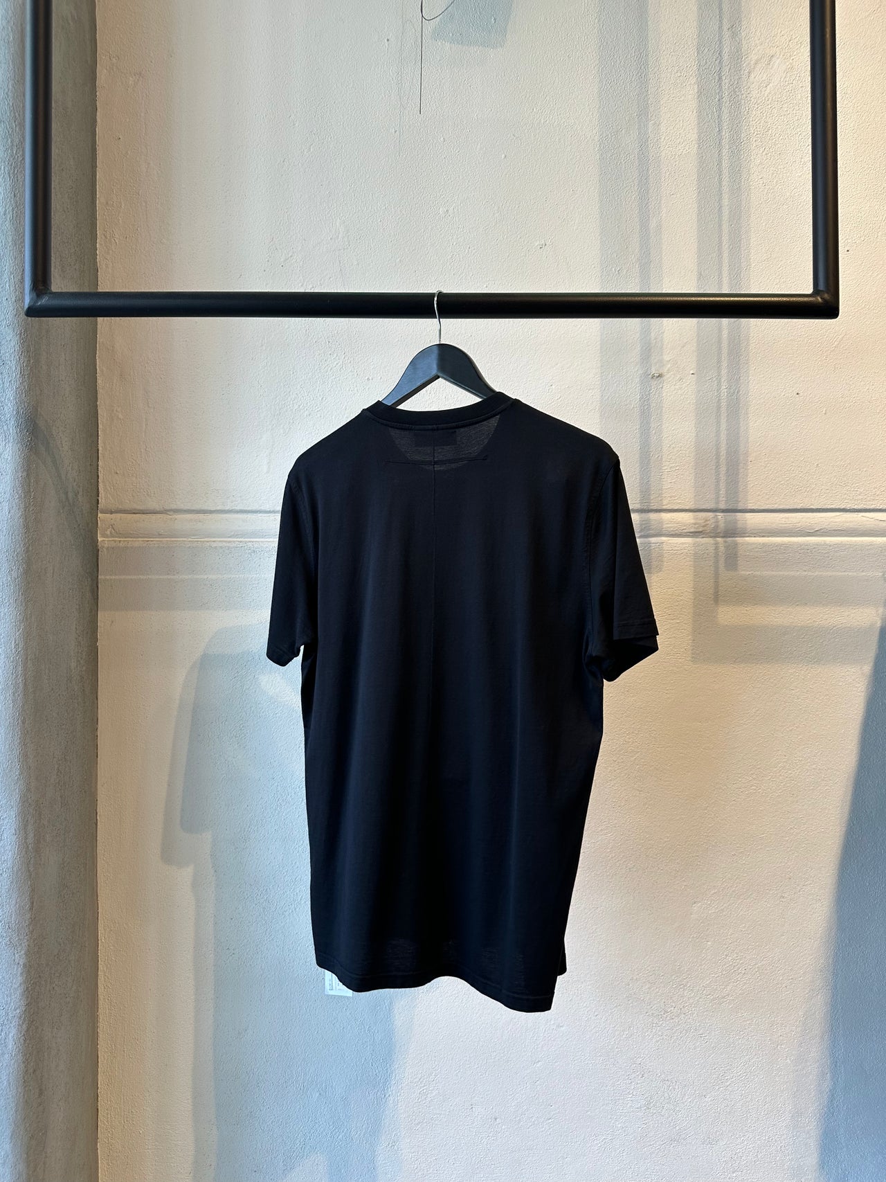 Black Givenchy t-shirt with a red and white graphic on a hanger against a neutral wall.