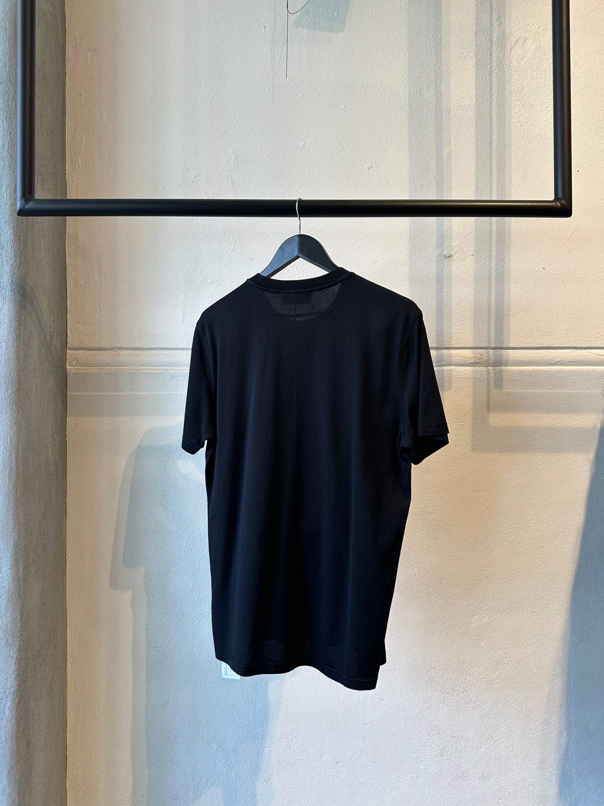 Black Givenchy t-shirt hanging on a hanger against a neutral wall.