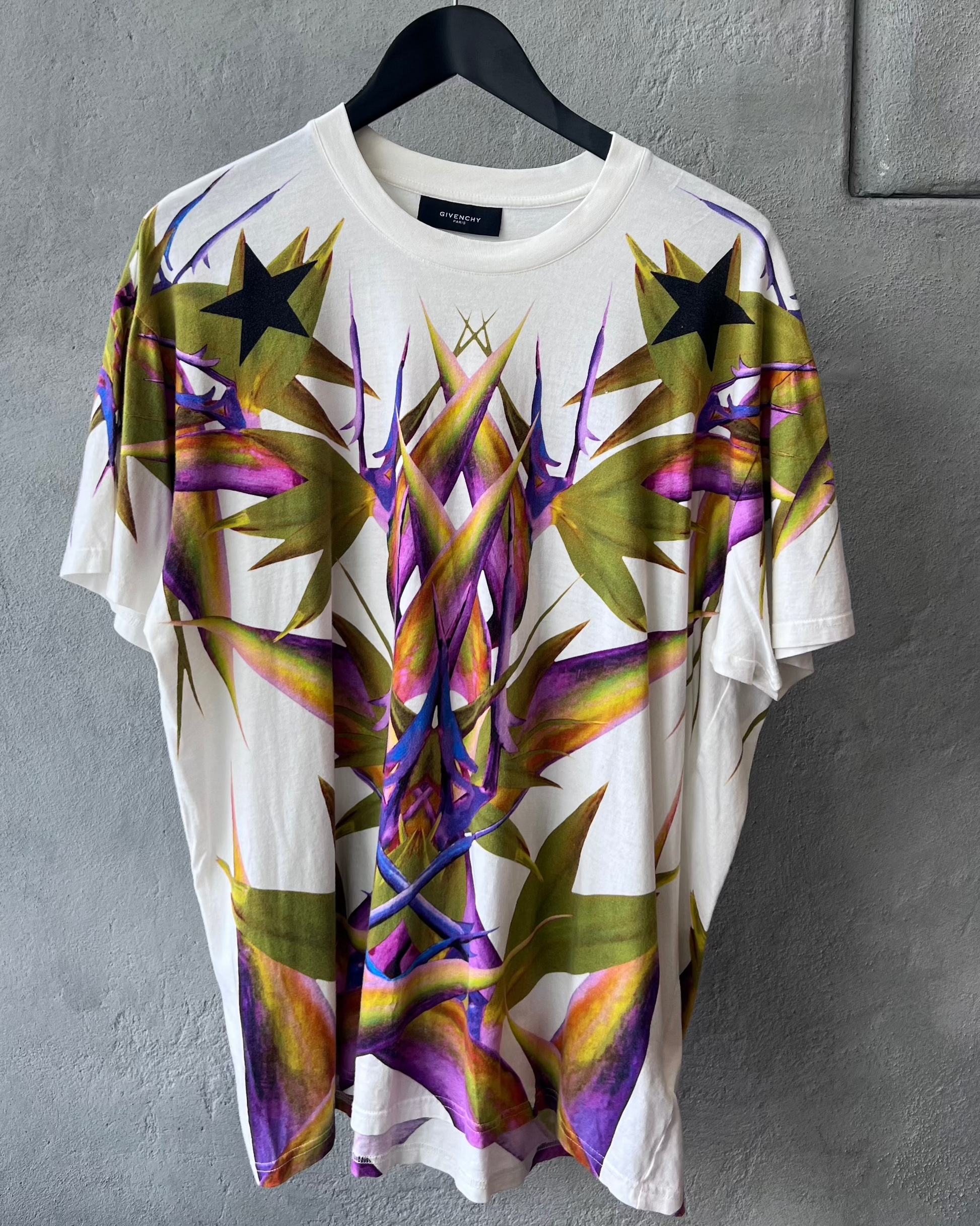 White Givenchy t-shirt with colourful abstract design on a hanger against a gray wall.