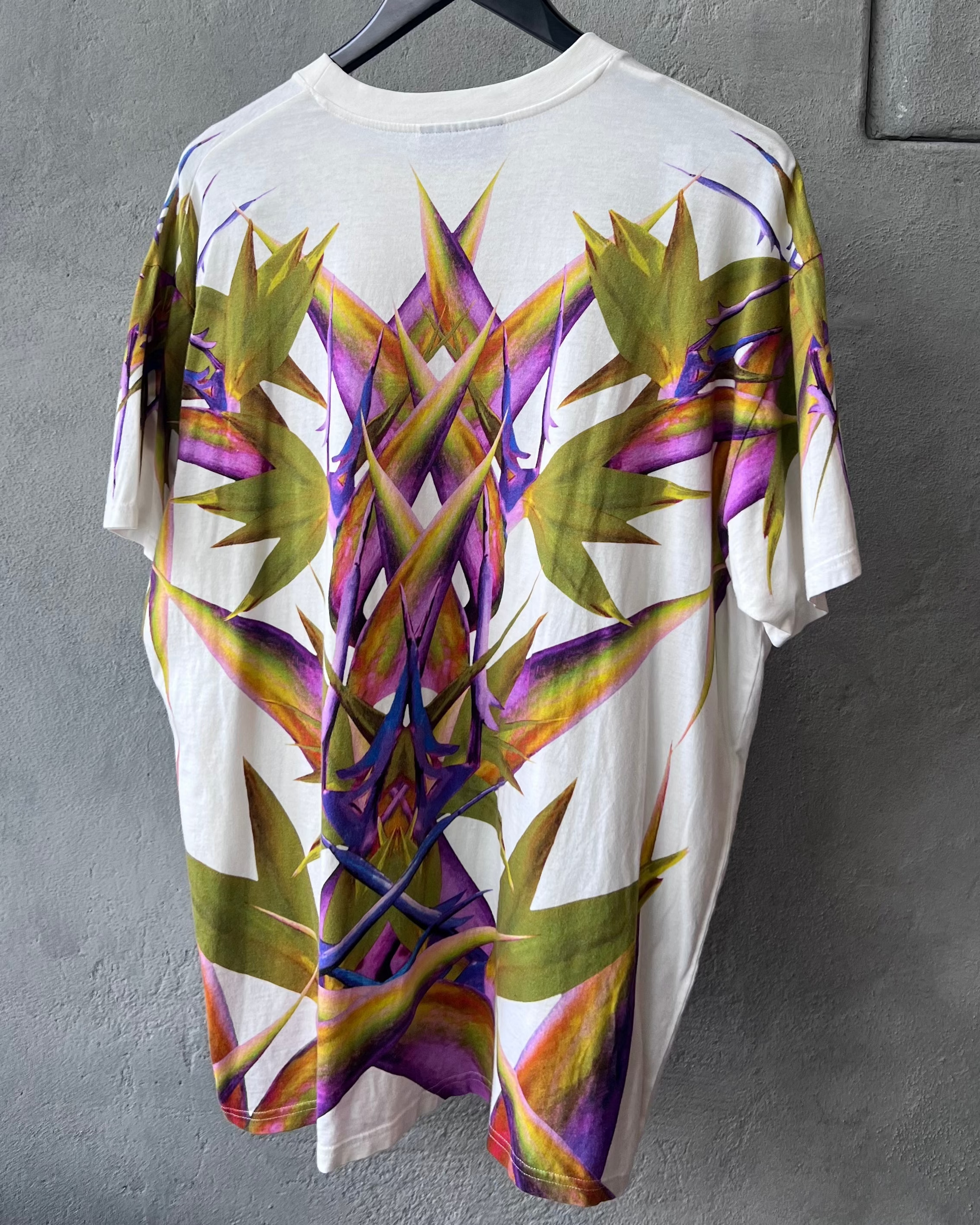 White Givenchy t-shirt with colourful floral design hanging on a gray wall.