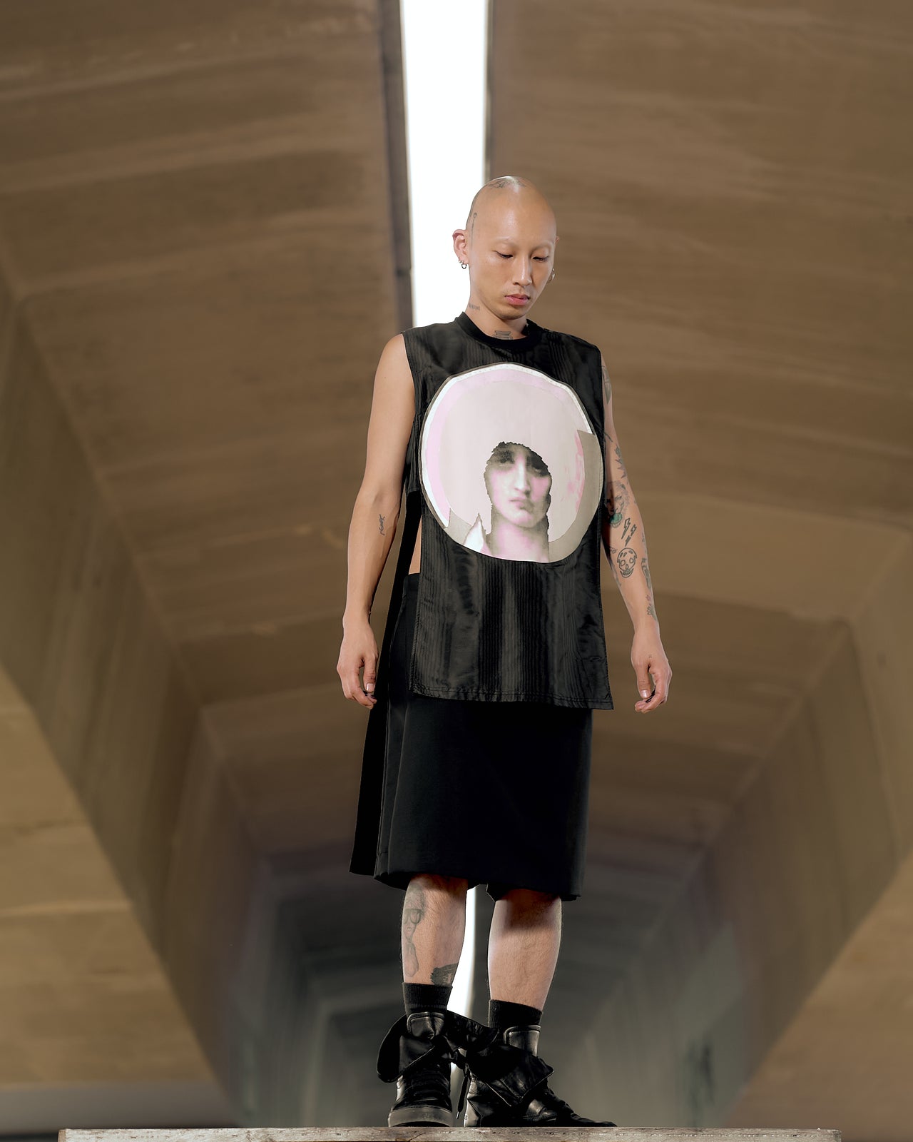 A male model wearing a sleeveless black Givenchy tank top with a graphic screen print of the Mother of Christ on the chest, standing in a tunnel-like setting.