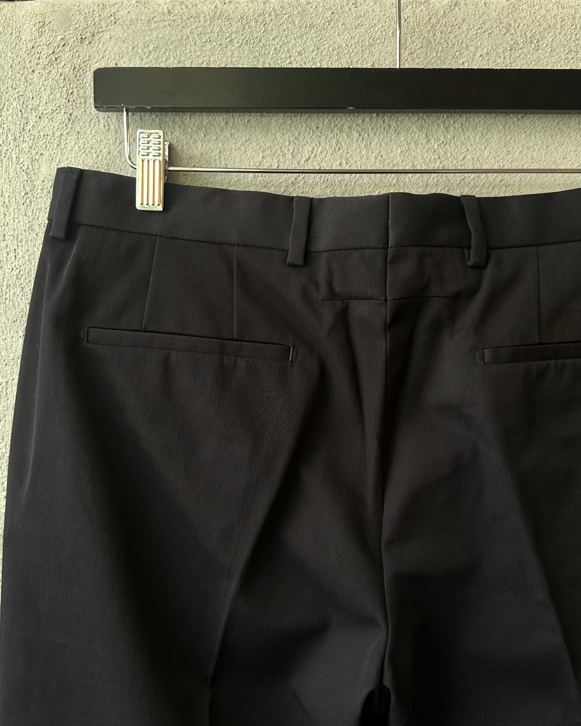 Black Givenchy pants hanging on a rack against a neutral wall.