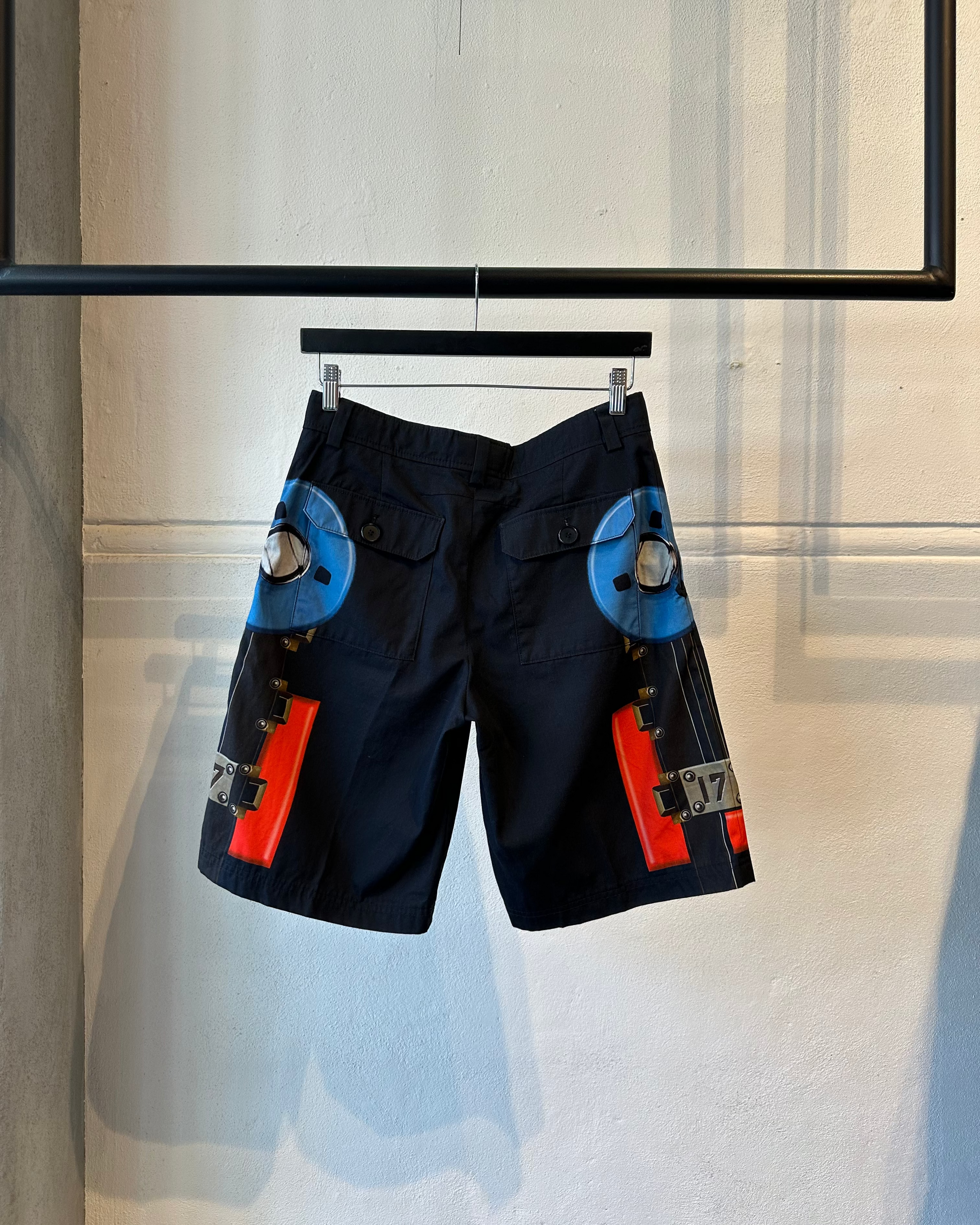 Black Givenchy shorts with blue and orange accents on a hanger against a neutral background