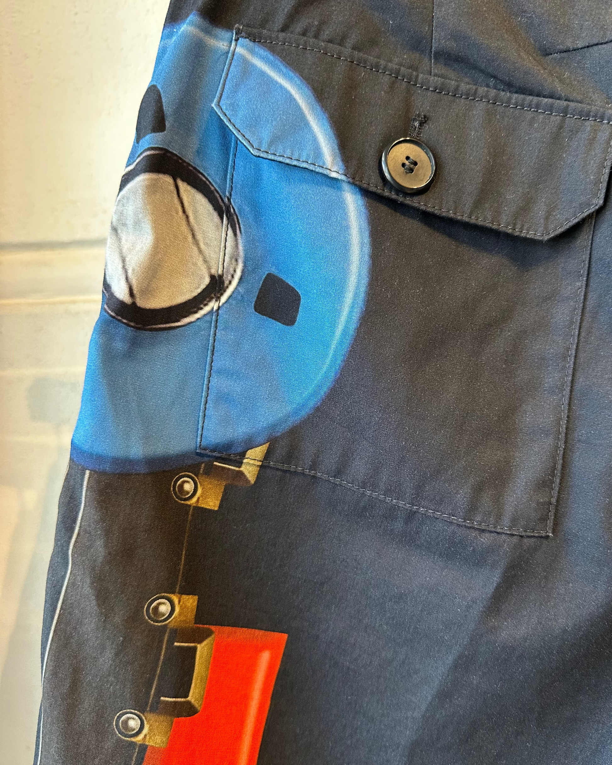 Close-up of a blue pocket on dark Givenchy shorts with a button and a small object inside.