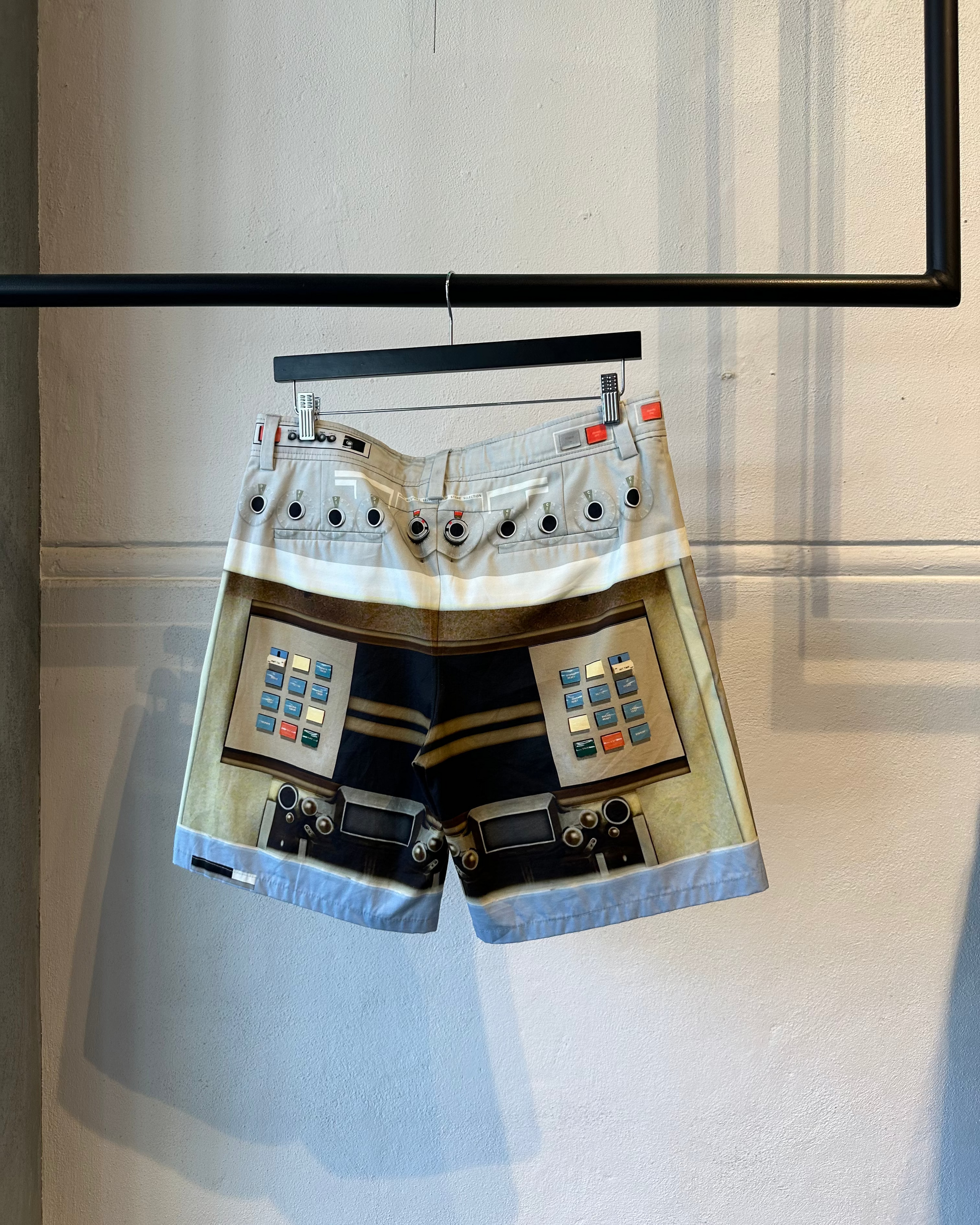 Reverse of Givenchy shorts with electronic device design on a hanger against a light background