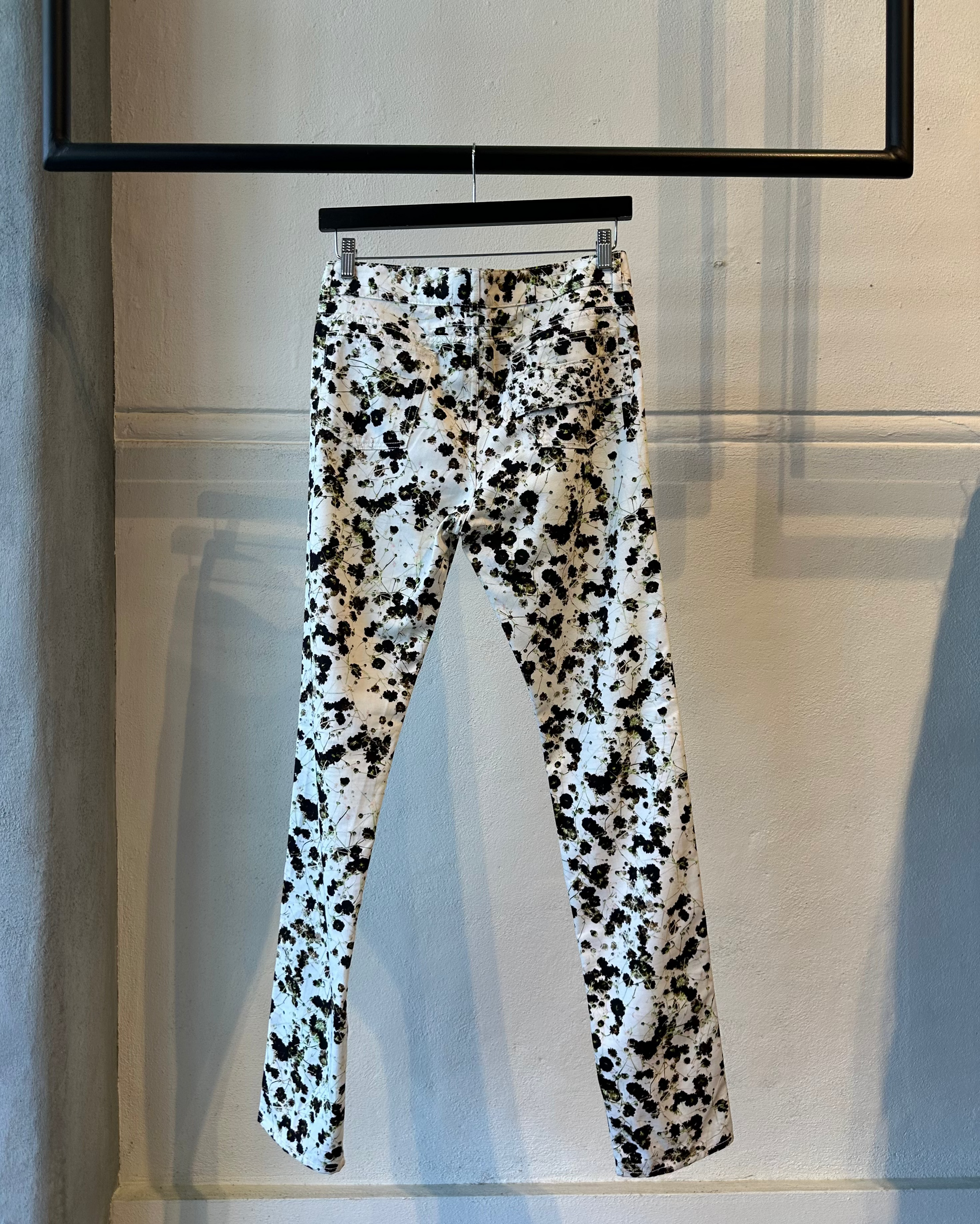 Black and white floral patterned pants Givenchy hanging on a rack against a neutral wall.