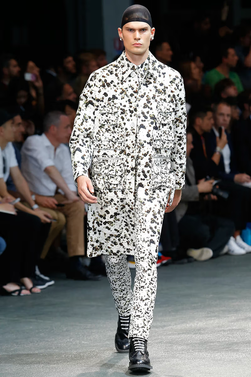 Model wearing a black and white patterned floral Givenchy outfit on a runway with an audience.
