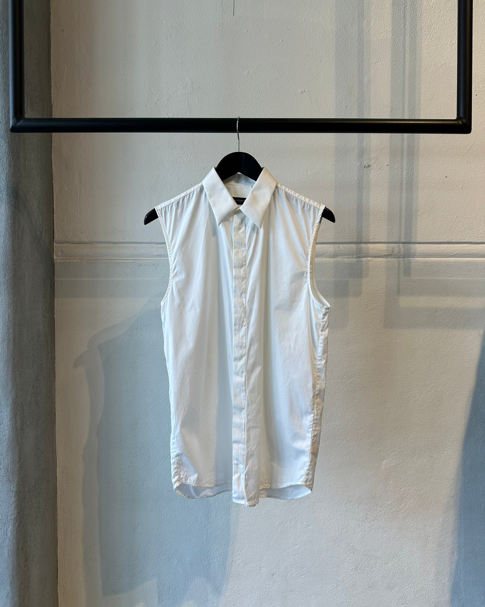 White sleeveless Givenchy shirt on a hanger against a light-colored wall.