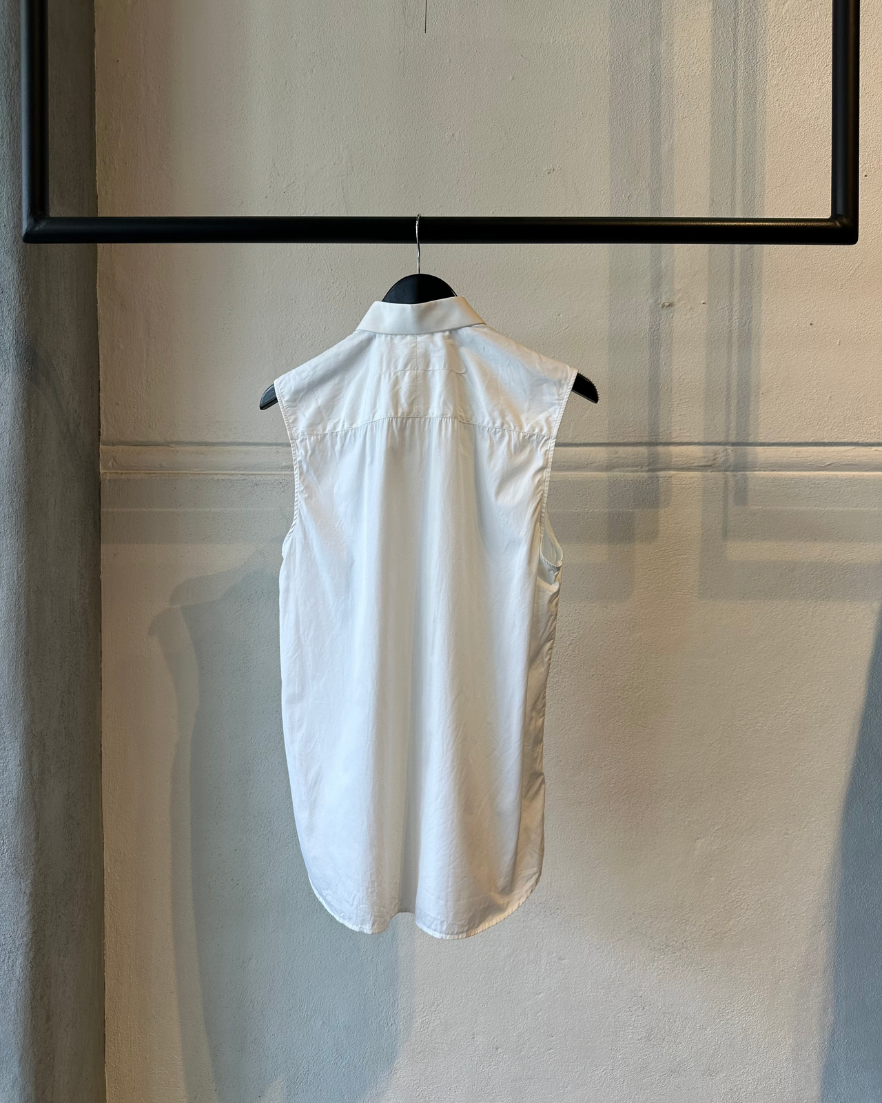White sleeveless Givenchy shirt on a hanger against a light-colored wall.