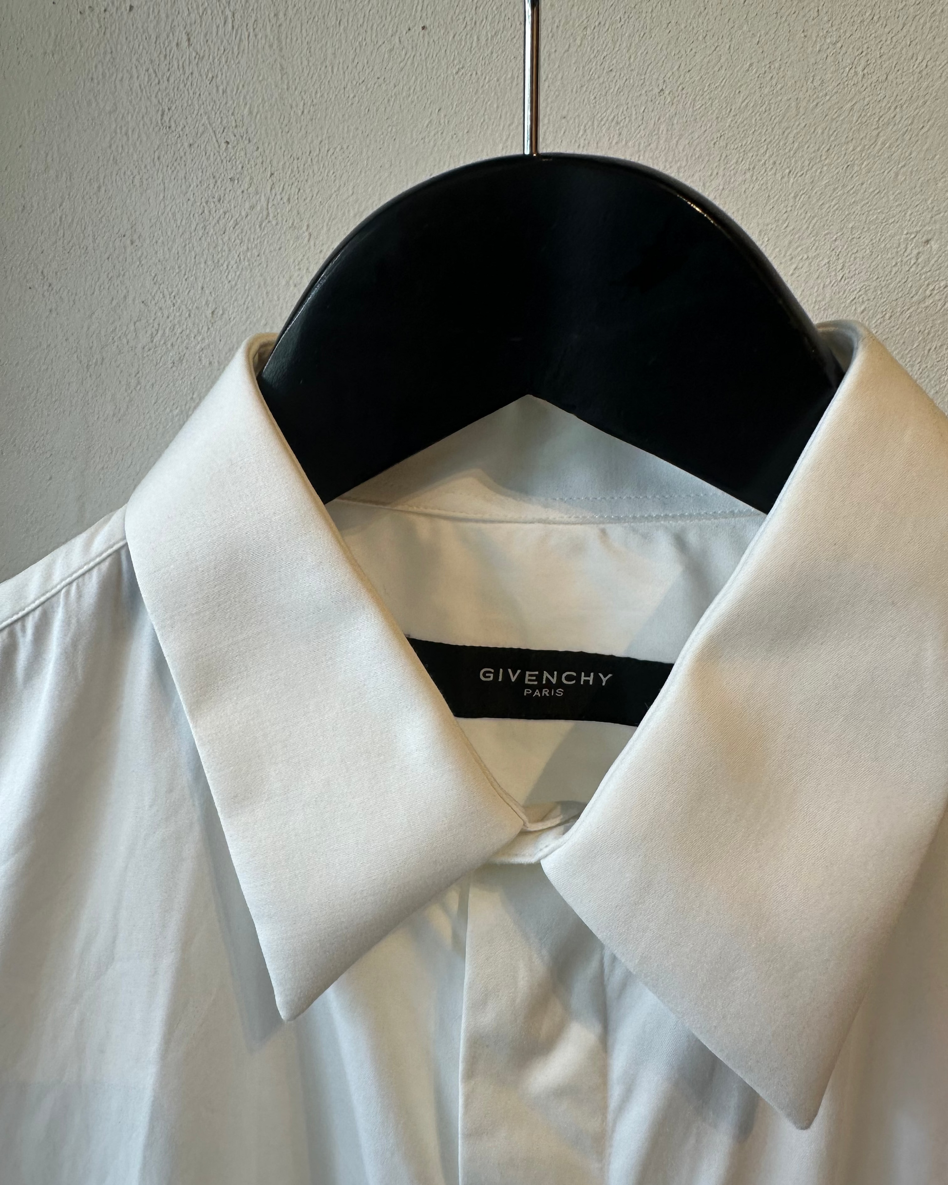 White shirt with Givenchy label on a black hanger against a beige wall.