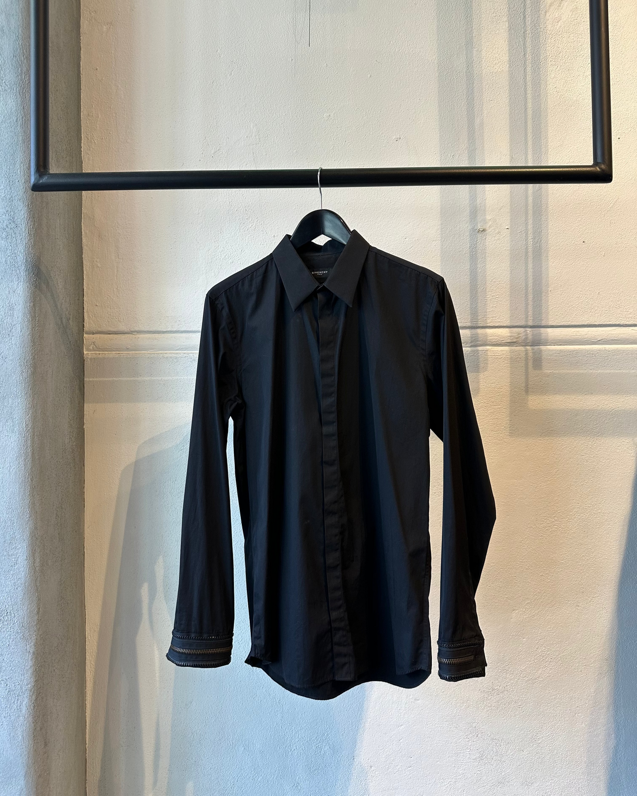 Black Givenchy shirt on a hanger against a neutral wall