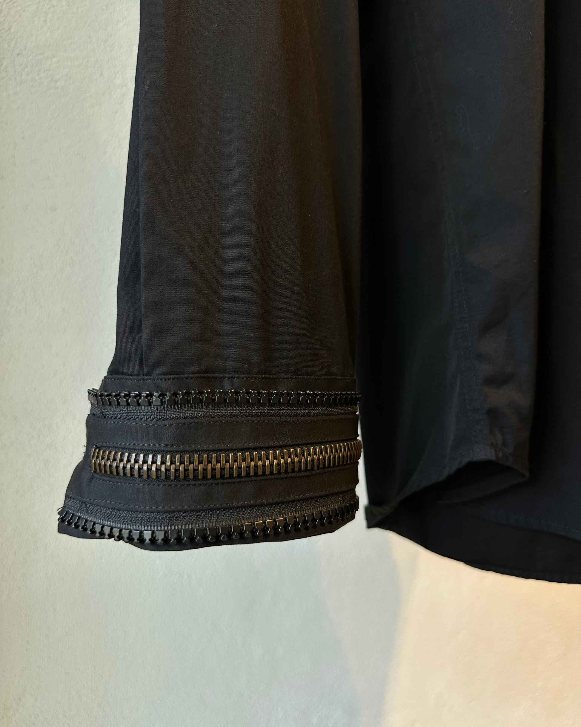 Close-up of a black Givenchy shirt sleeve with zippers with textured trim on a neutral background