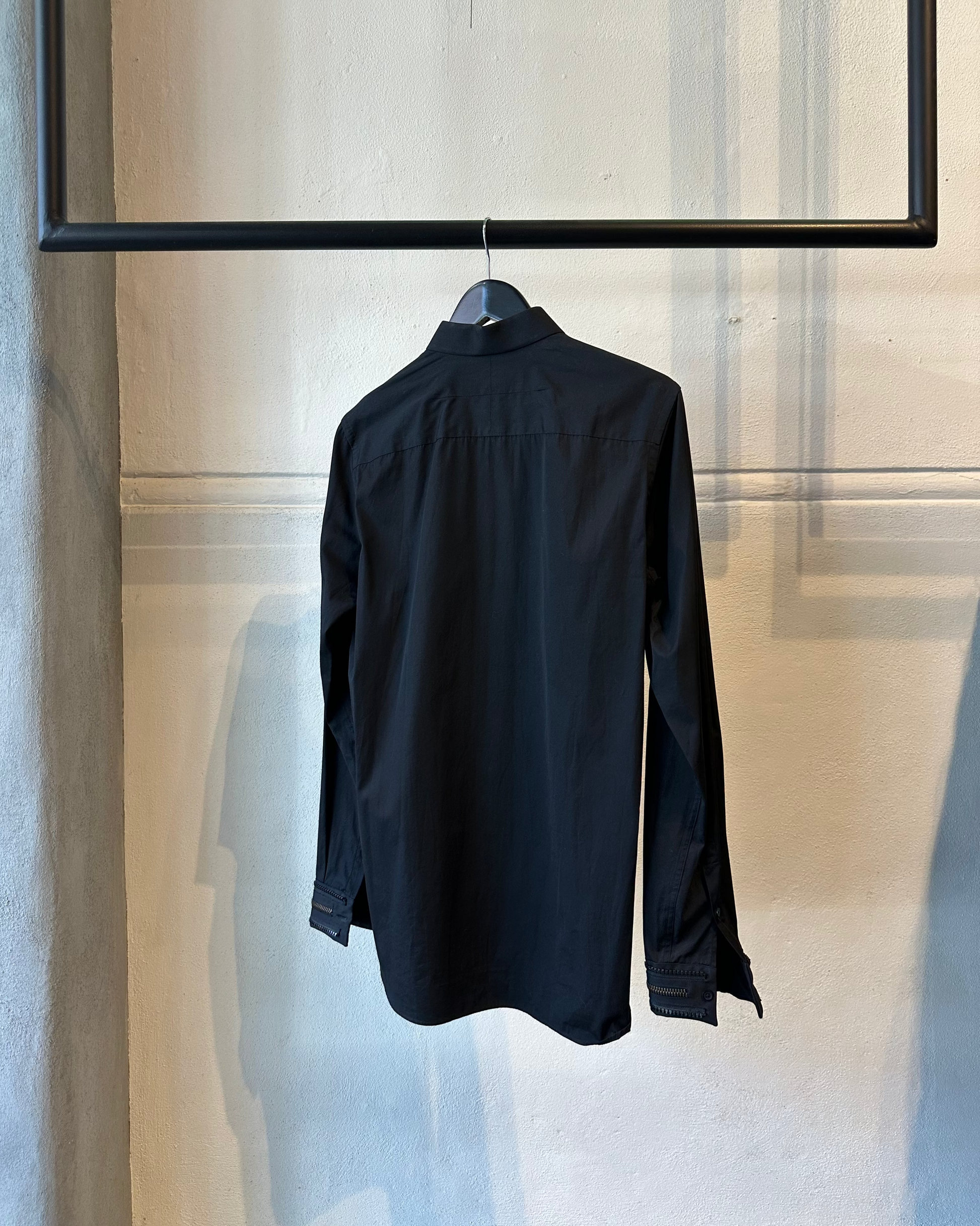 Reverse of a black Givenchy shirt on a hanger against a neutral wall
