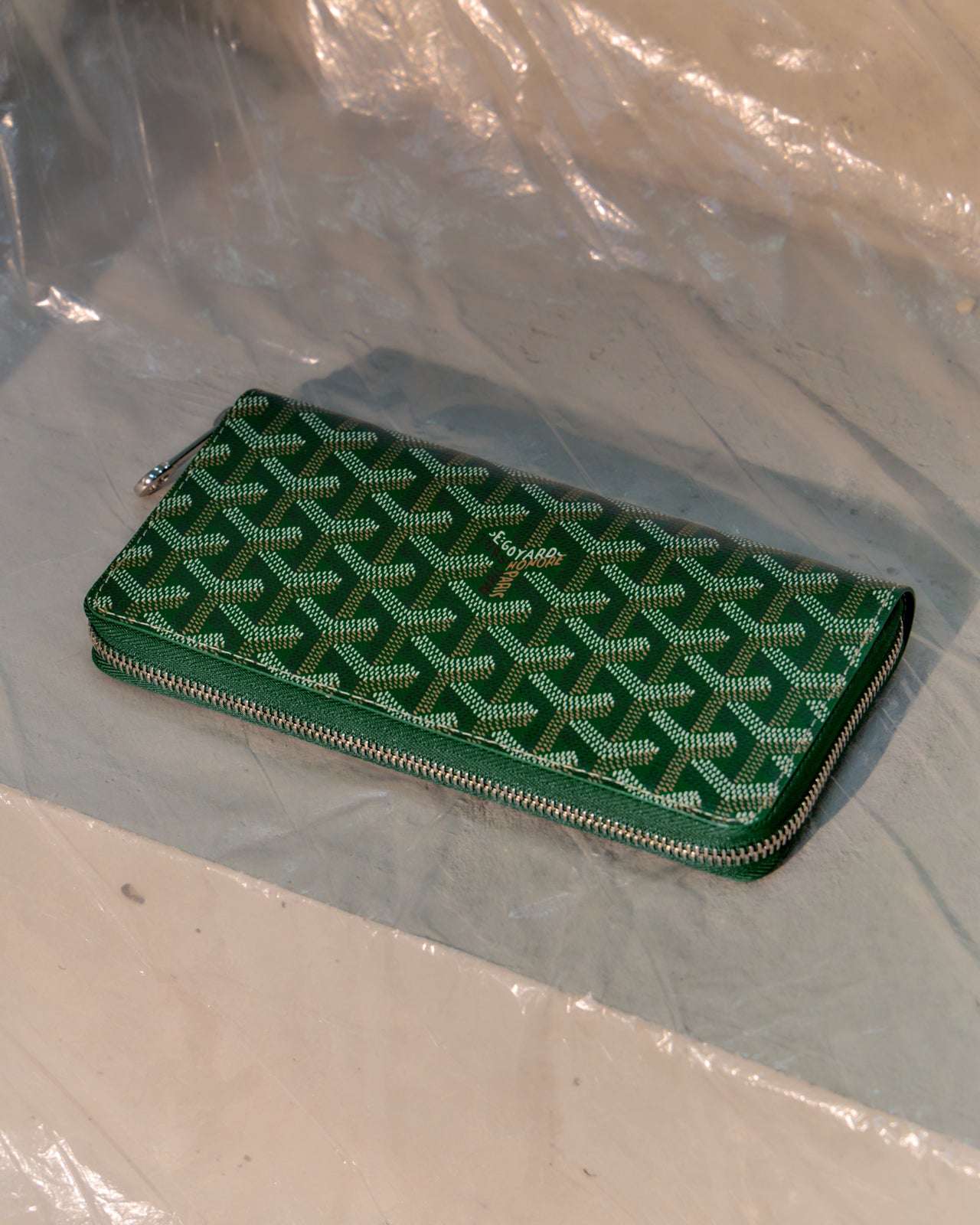 Green Goyard patterned wallet on a clear plastic sheet