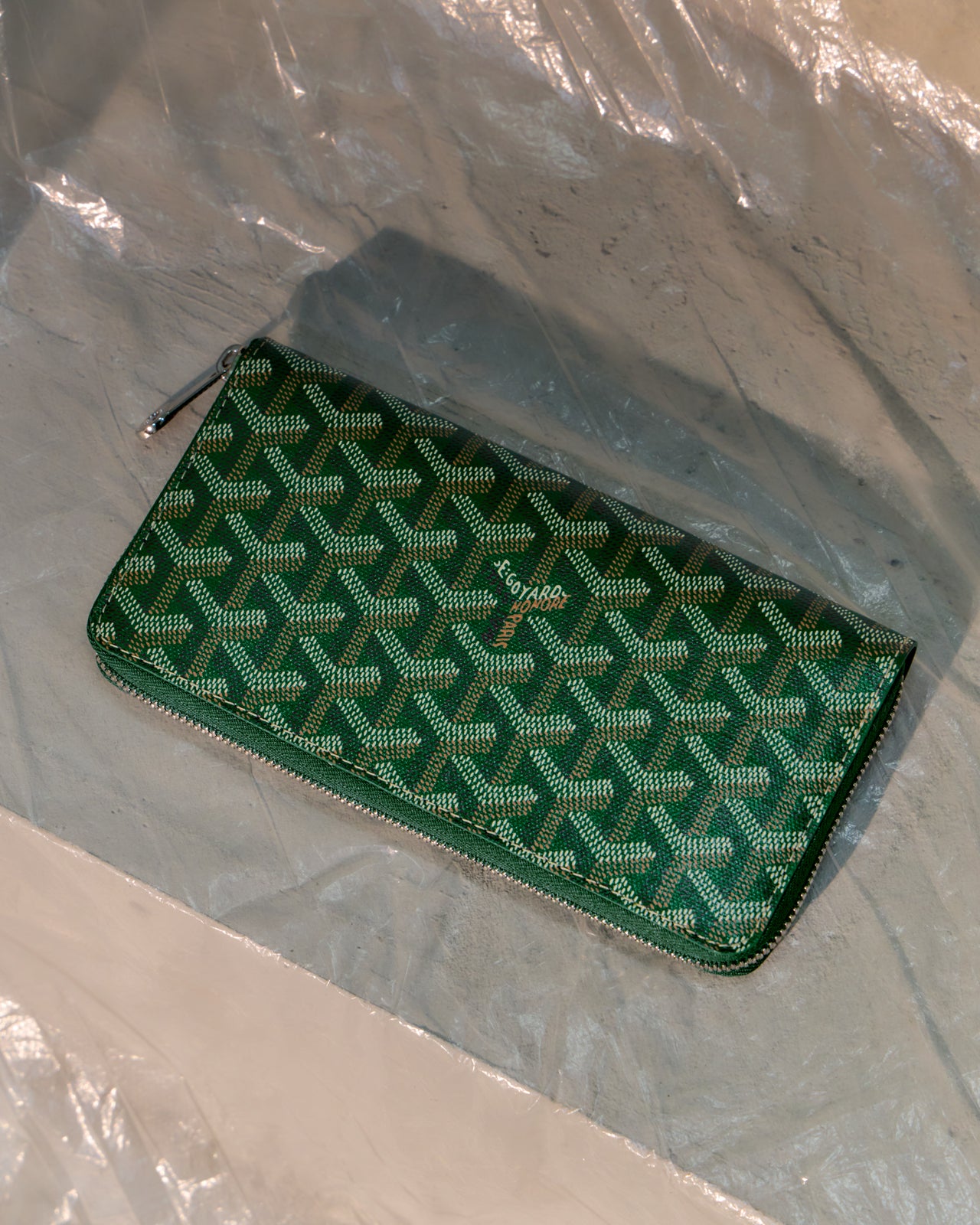 Green Goyard patterned wallet on a clear plastic sheet