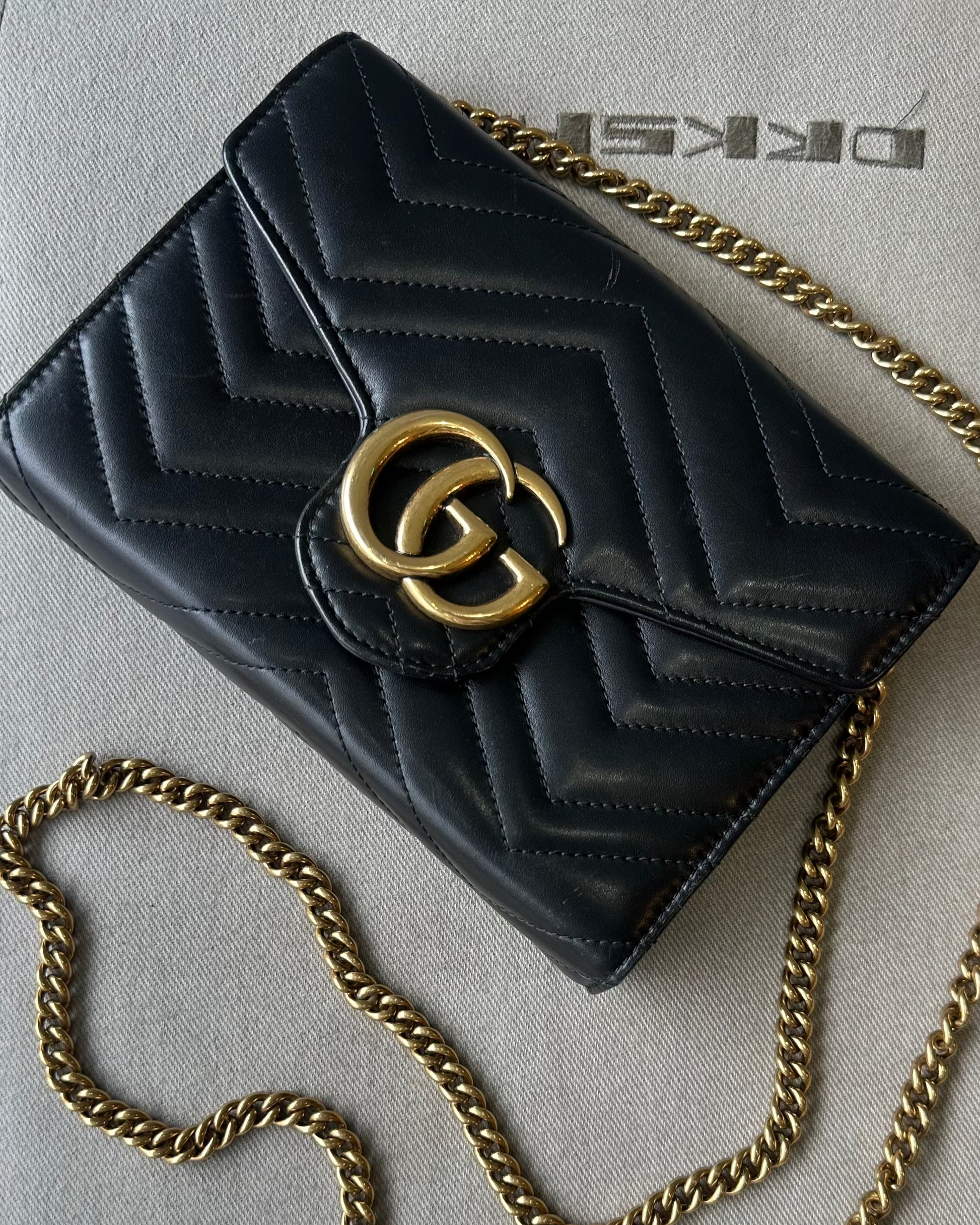 Black quilted Gucci handbag with gold chain and logo on a light gray background