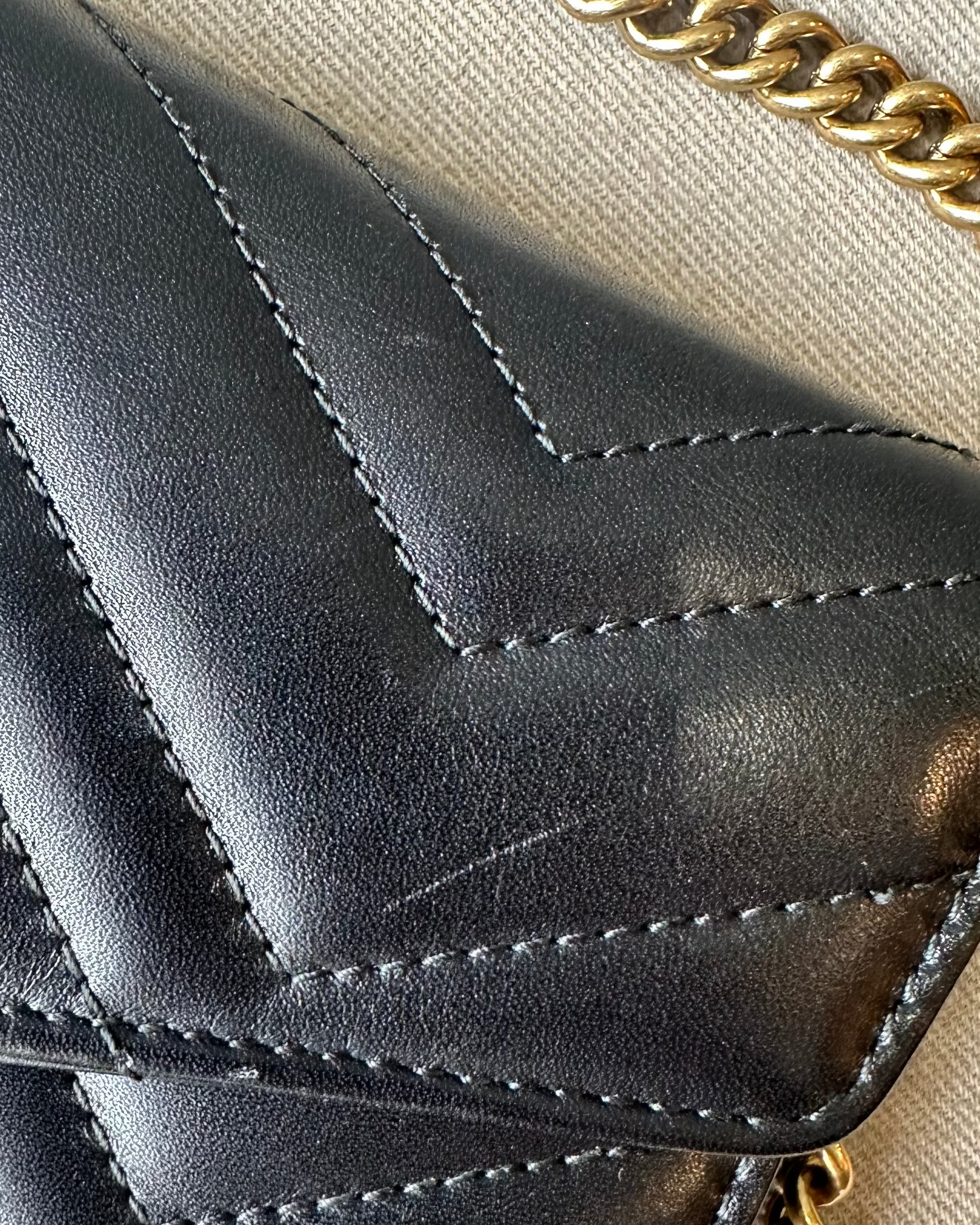 Close-up of a black quilted Gucci handbag with gold chain strap on a beige background