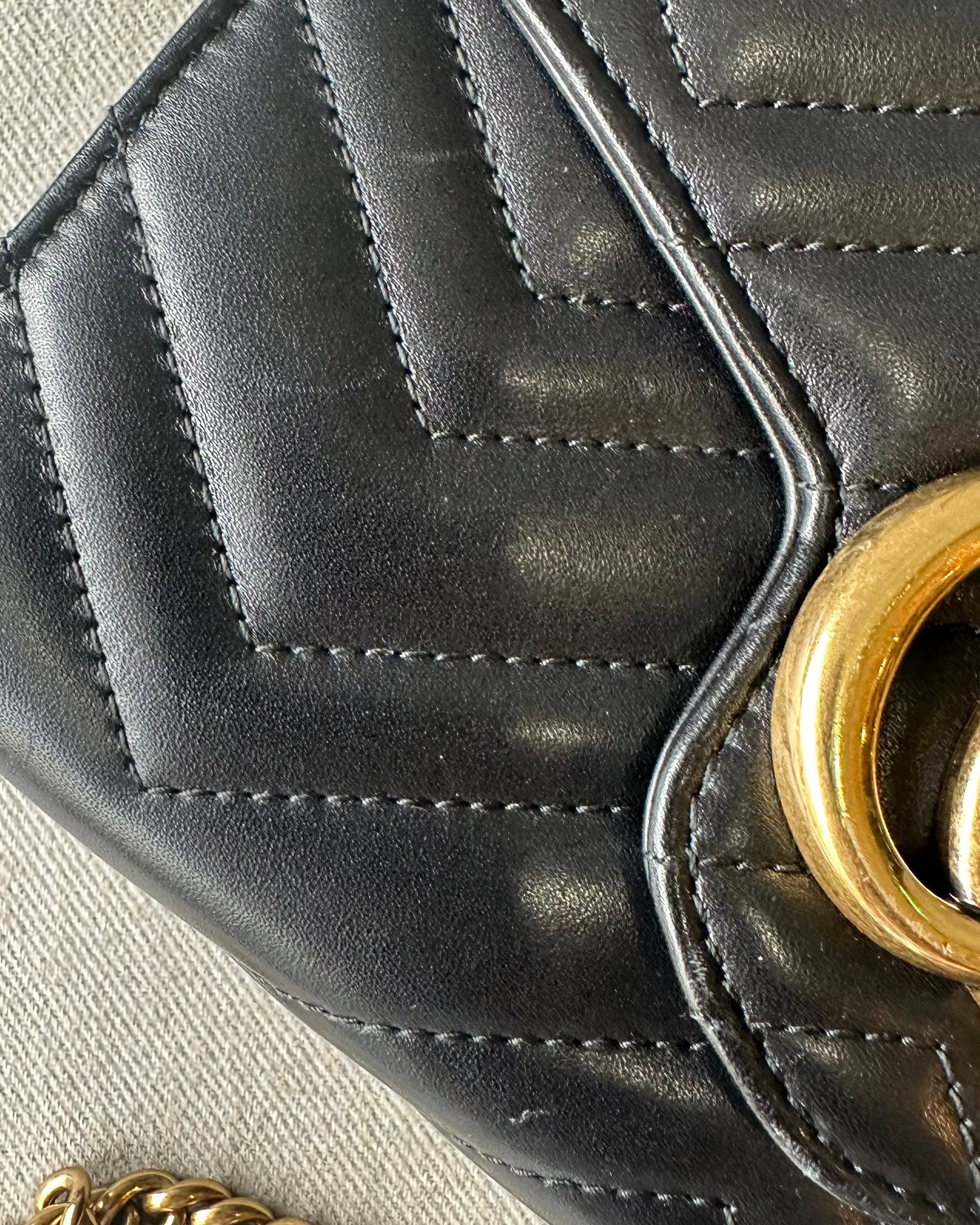 Black quilted Gucci handbag with gold chain on a light gray background