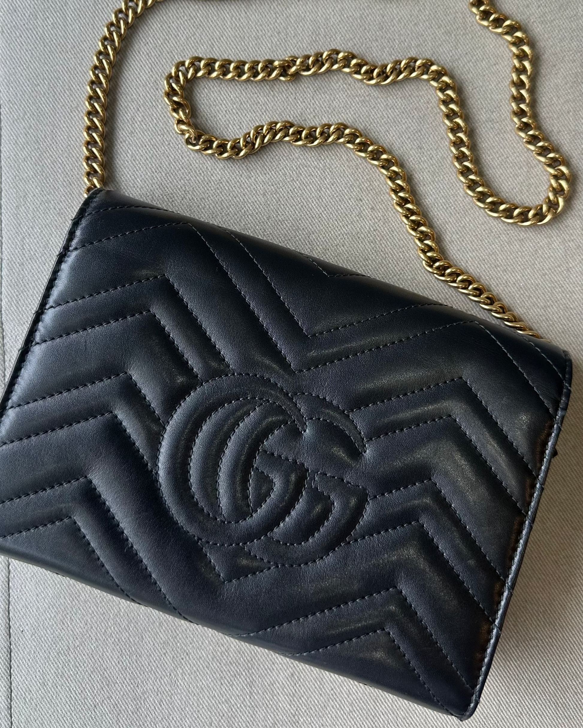 Black quilted Gucci handbag with gold chain on a light gray background