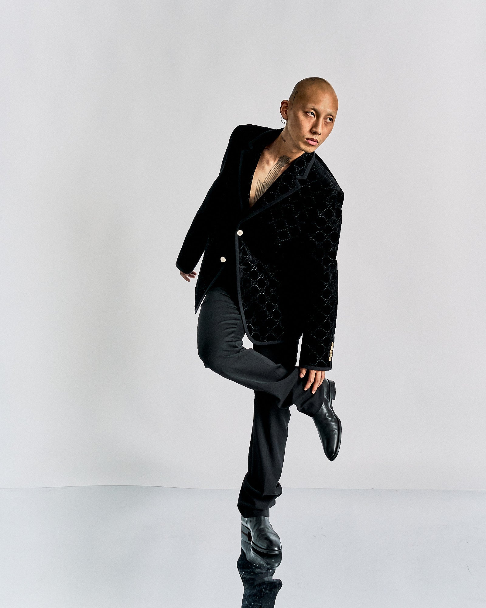 Person in a stylish black Gucci velvet jacket and black pants, posed dynamically with one knee bent and head tilted.