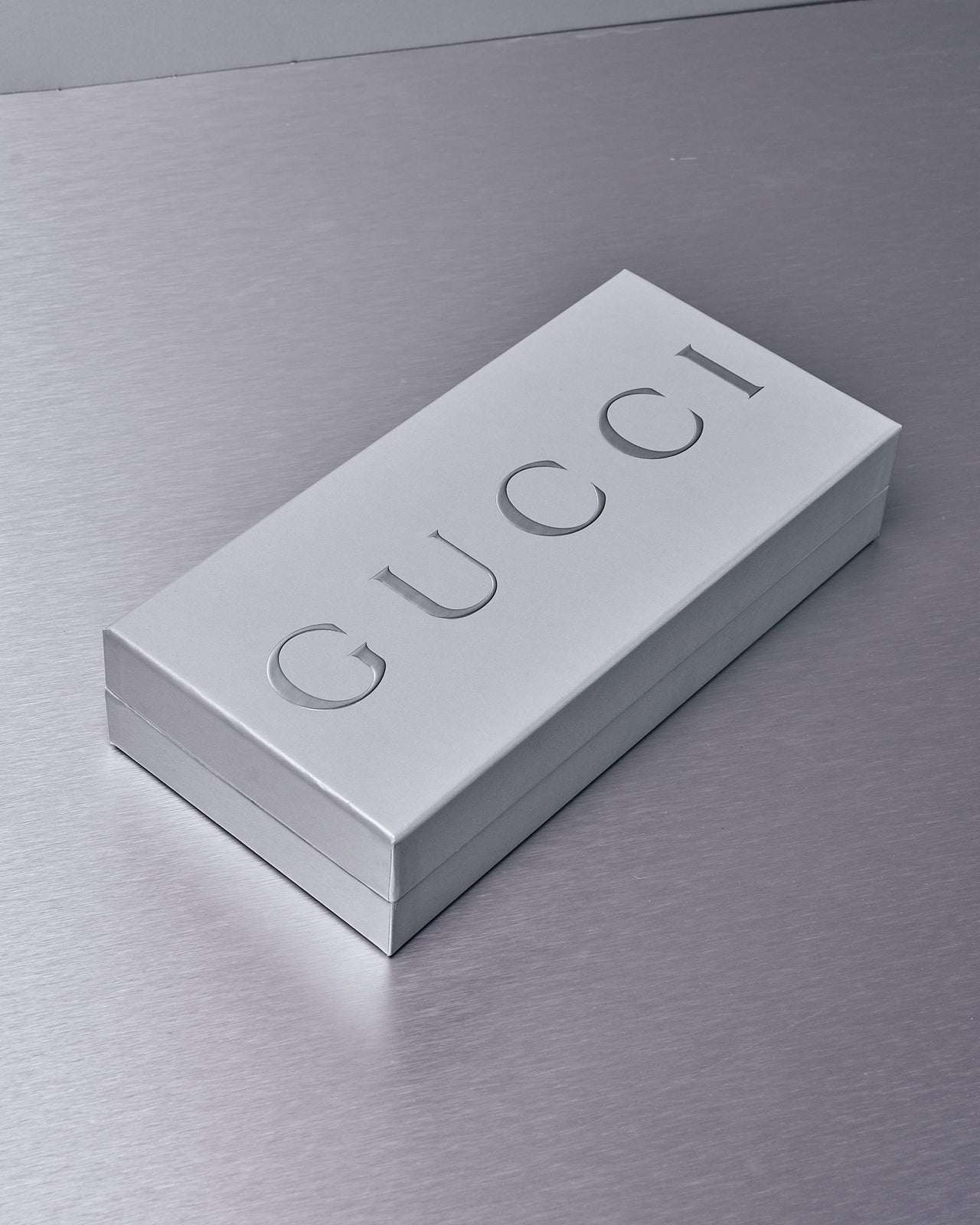 A large deck of Ace of Hearts Gucci playing cards sits beside a small green leather cardholder with gold detailing, on a metallic surface.