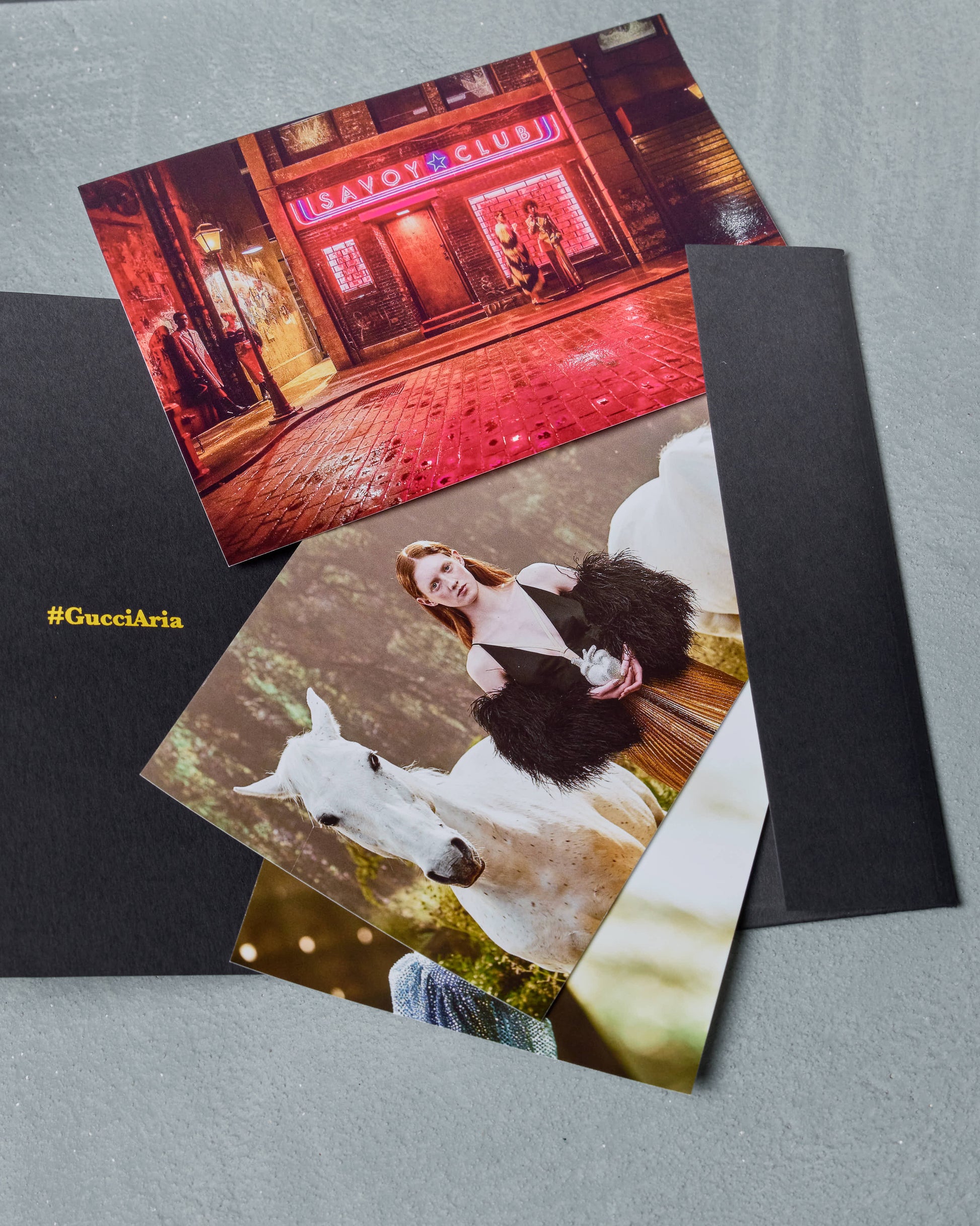 Two Gucci photo prints on black paper with a neon sign and a horse and person photo.