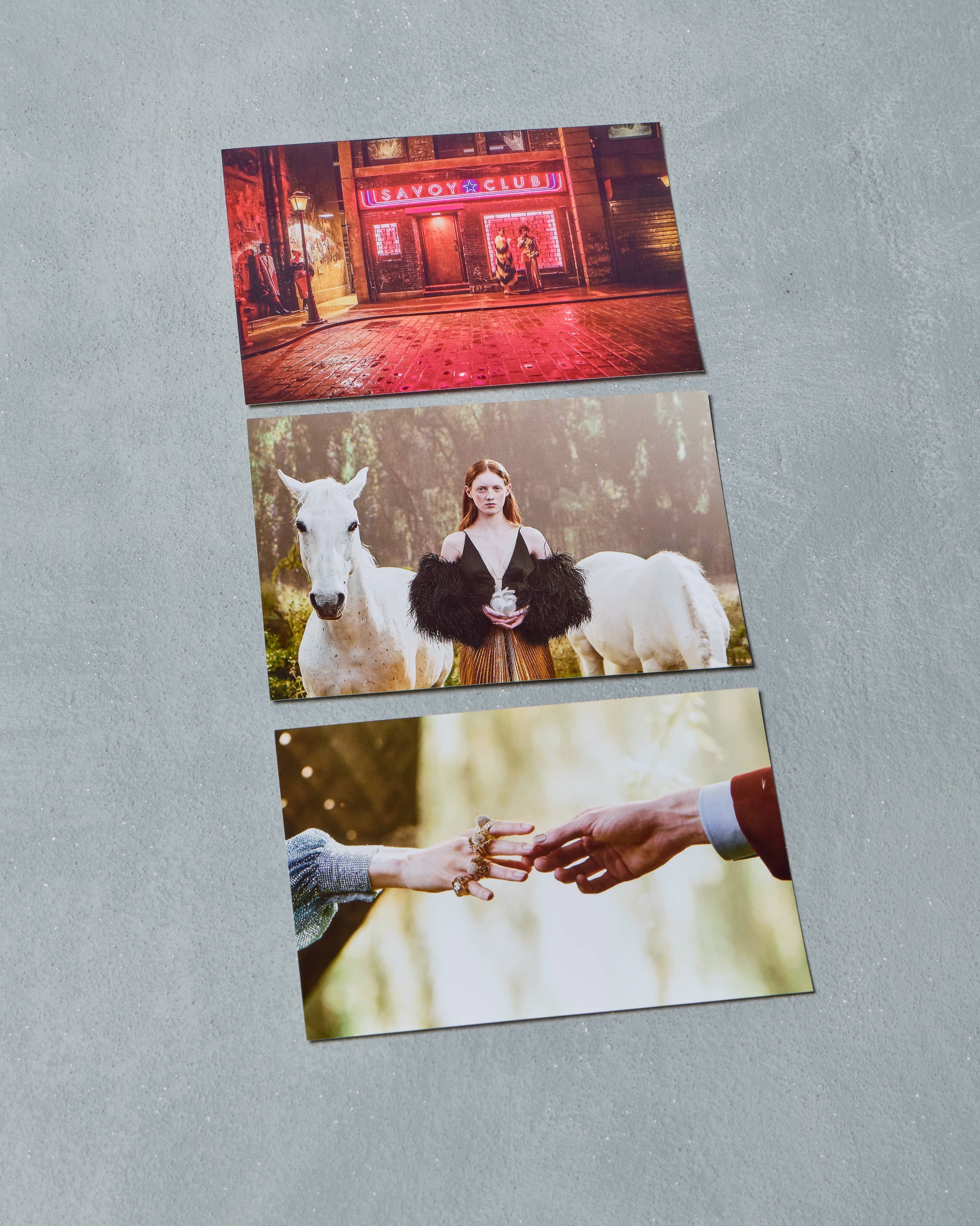 Three printed Gucci photos on a gray surface: a city street scene, a woman with a white horse, and two hands holding hands.