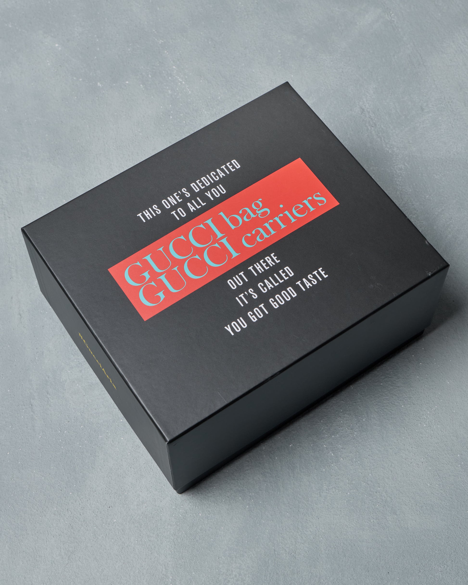Black Gucci box with red and white text on a gray background